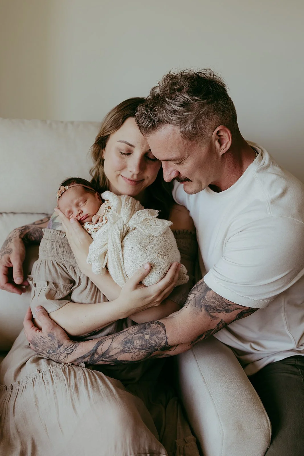 A family holding a newborn baby, with the mother and father close together, all smiling softly.