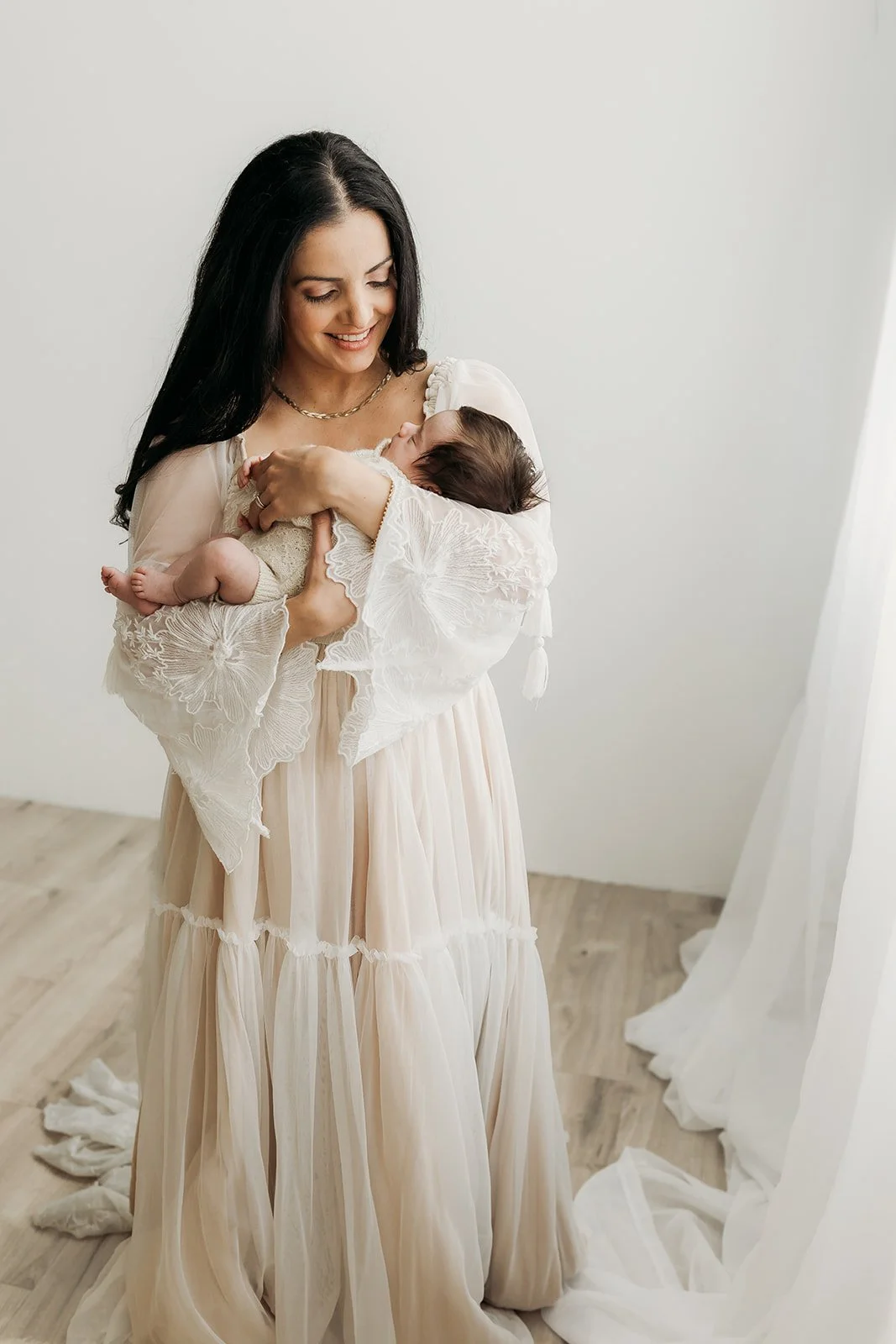 a woman in a white dress is holding her new baby girl during a newborn photo shoot with Ann Marie of AMG Photography