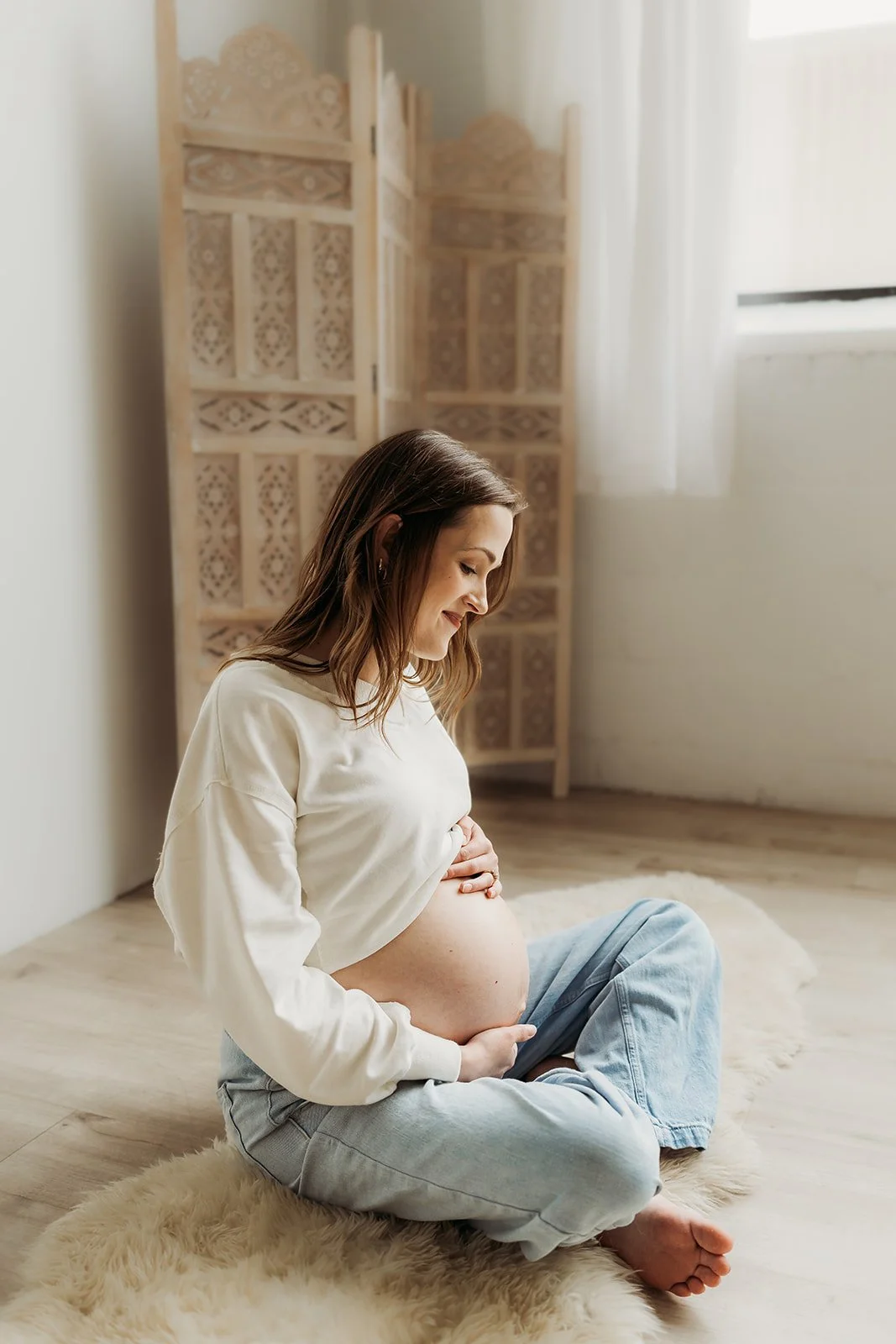 a young pregnant woman is holding her baby bump while relaxing on the floor at AMG Photography's studio in Minneapolis, MN