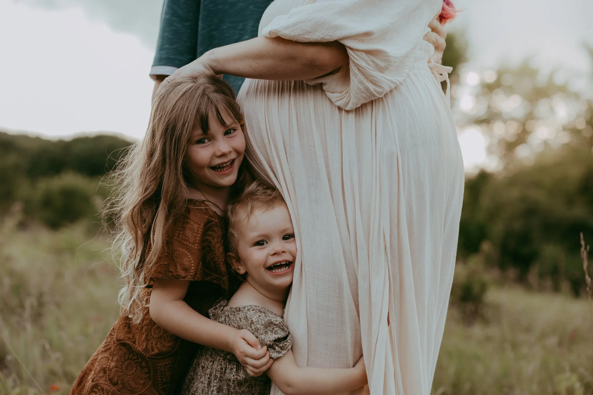 two little girls are hugging their pregnant momma during a maternity photo shoot with AMG Photography