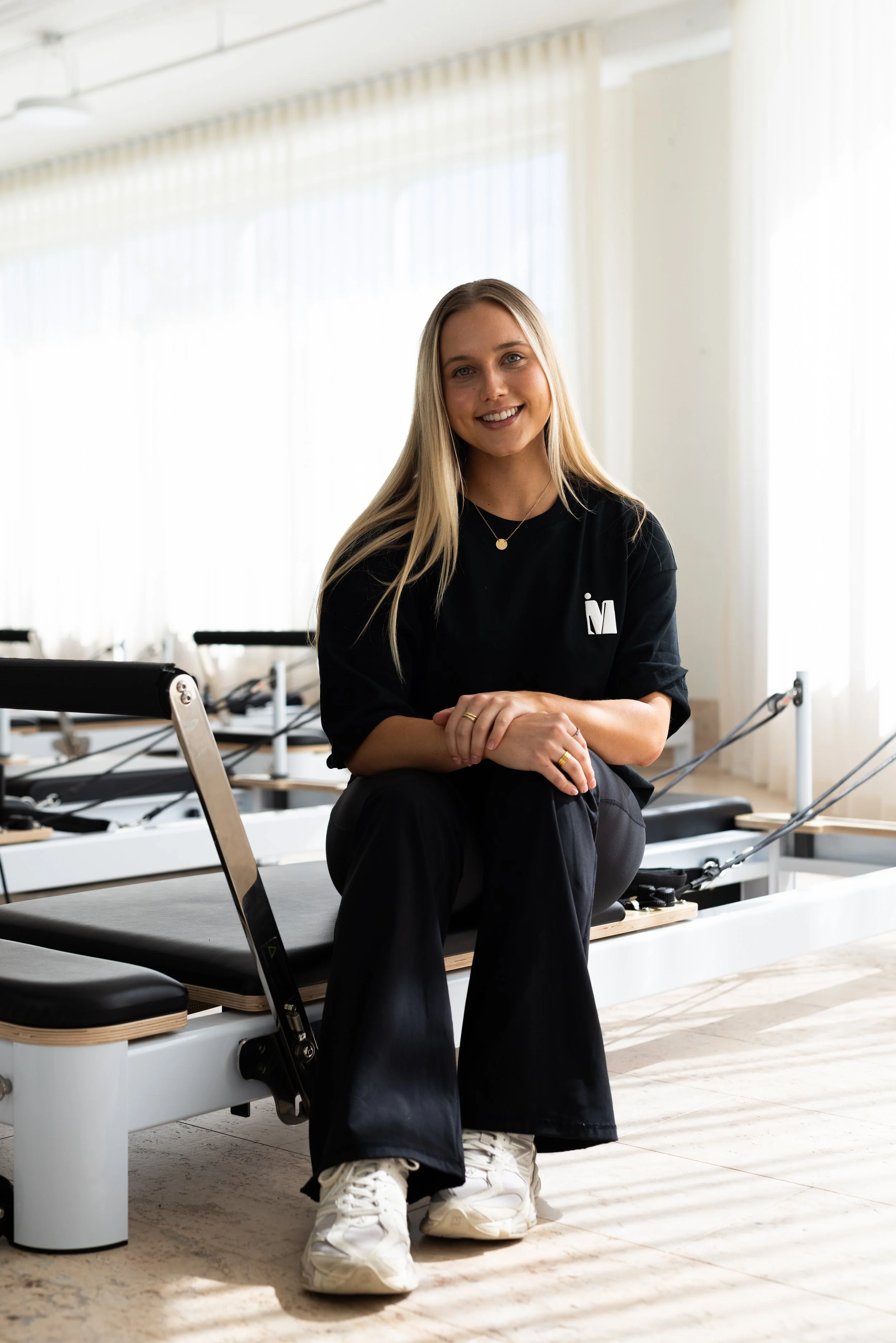A woman with long blond hair sitting on a pilates reformer machine