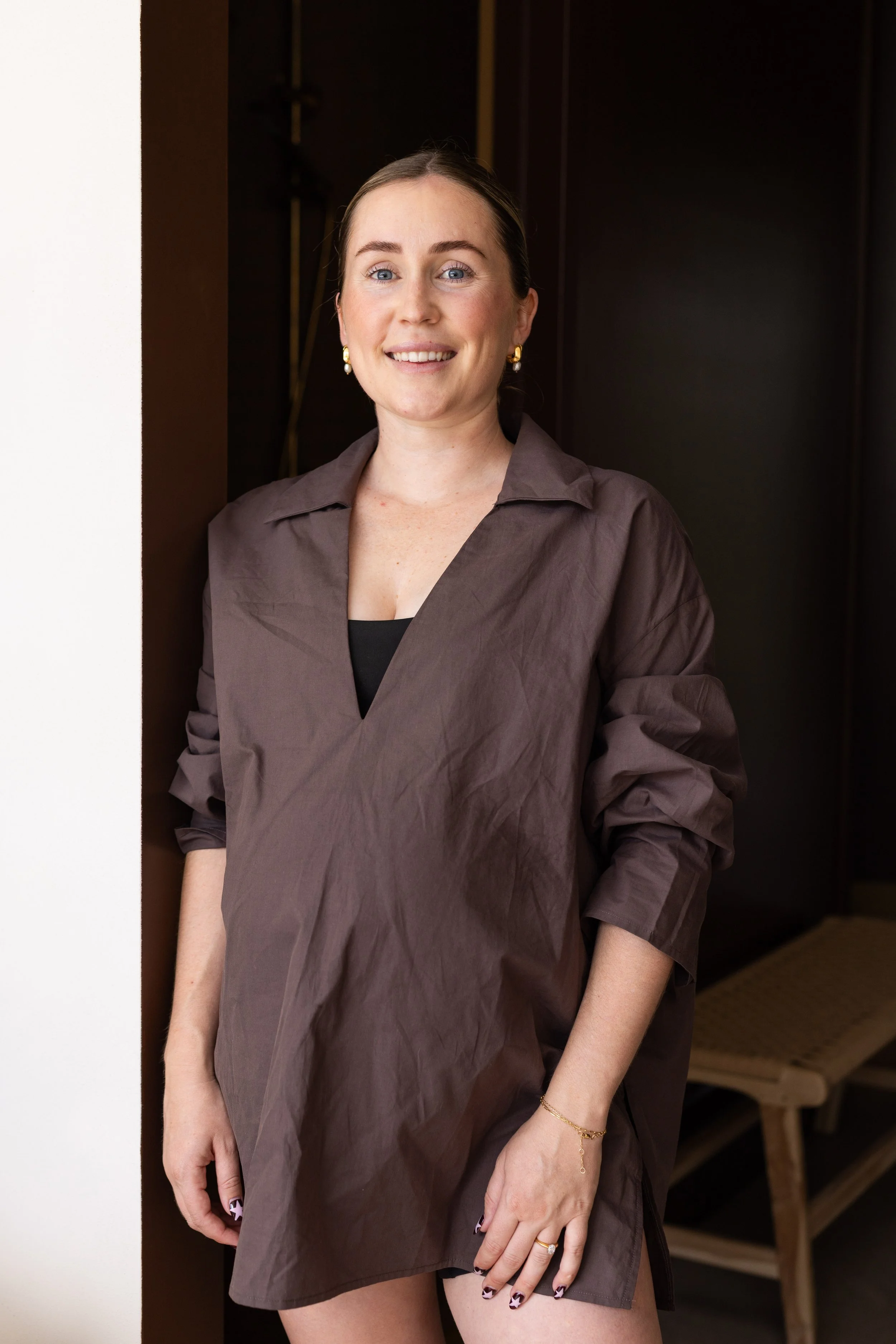A women with her hair pulled back, wearing a brown shirt standing in a doorway