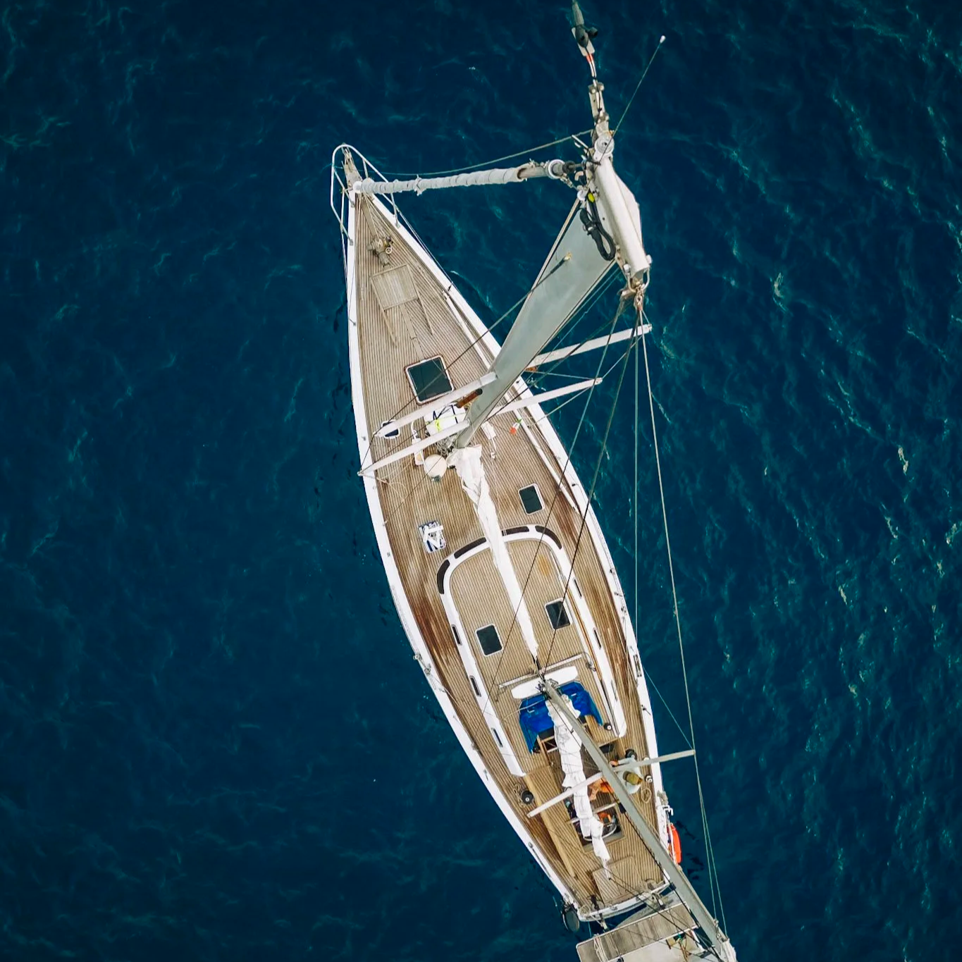 Overhead view of a sailboat on the ocean with a wooden deck, mast, and sails.