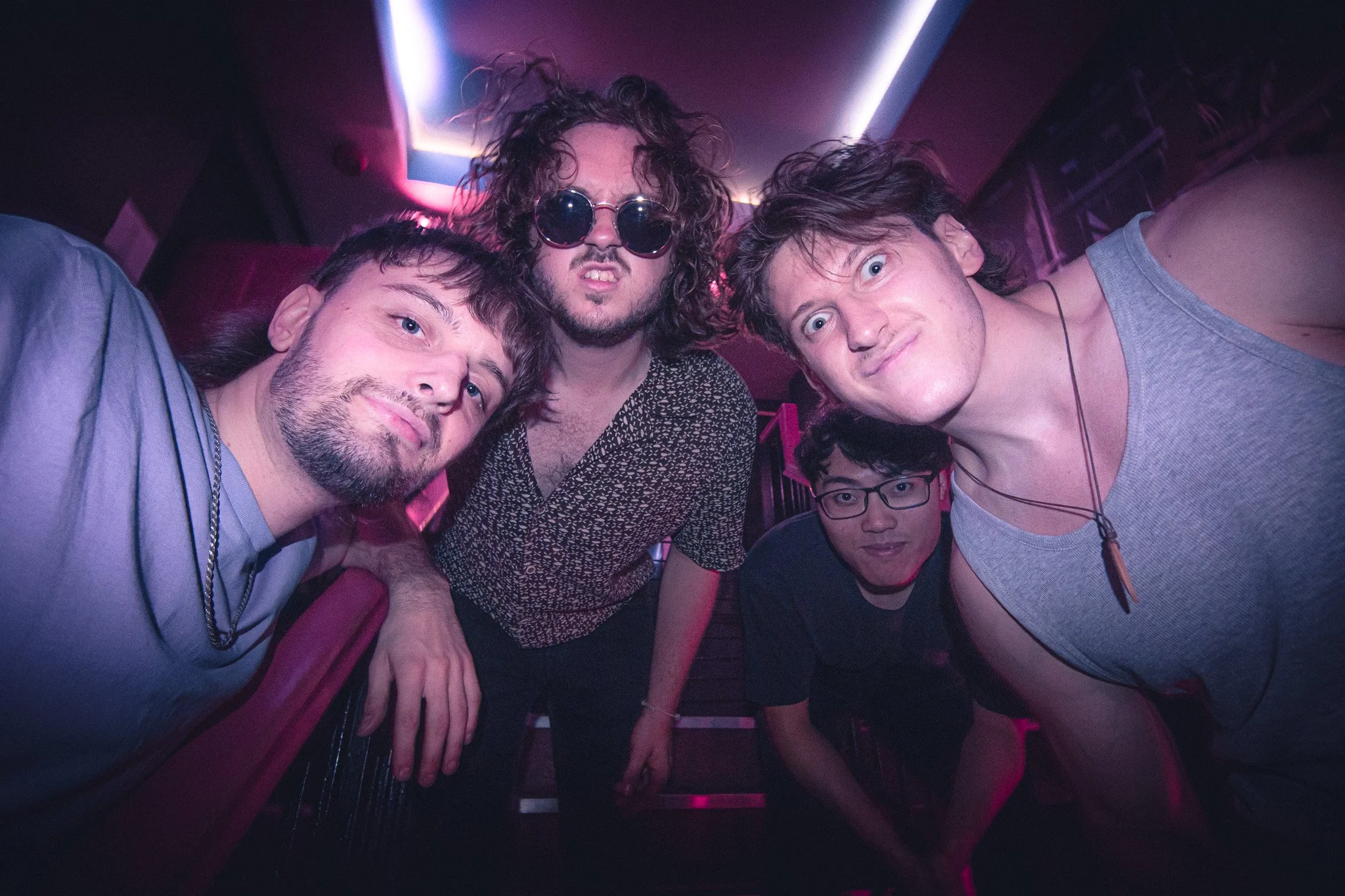 The Jetty's promo photo at the Dark Horse, Moseley, Birmingham. Five young men taking a selfie in a dimly lit club with pink and purple lighting, some with curly hair and glasses, posing closely together.