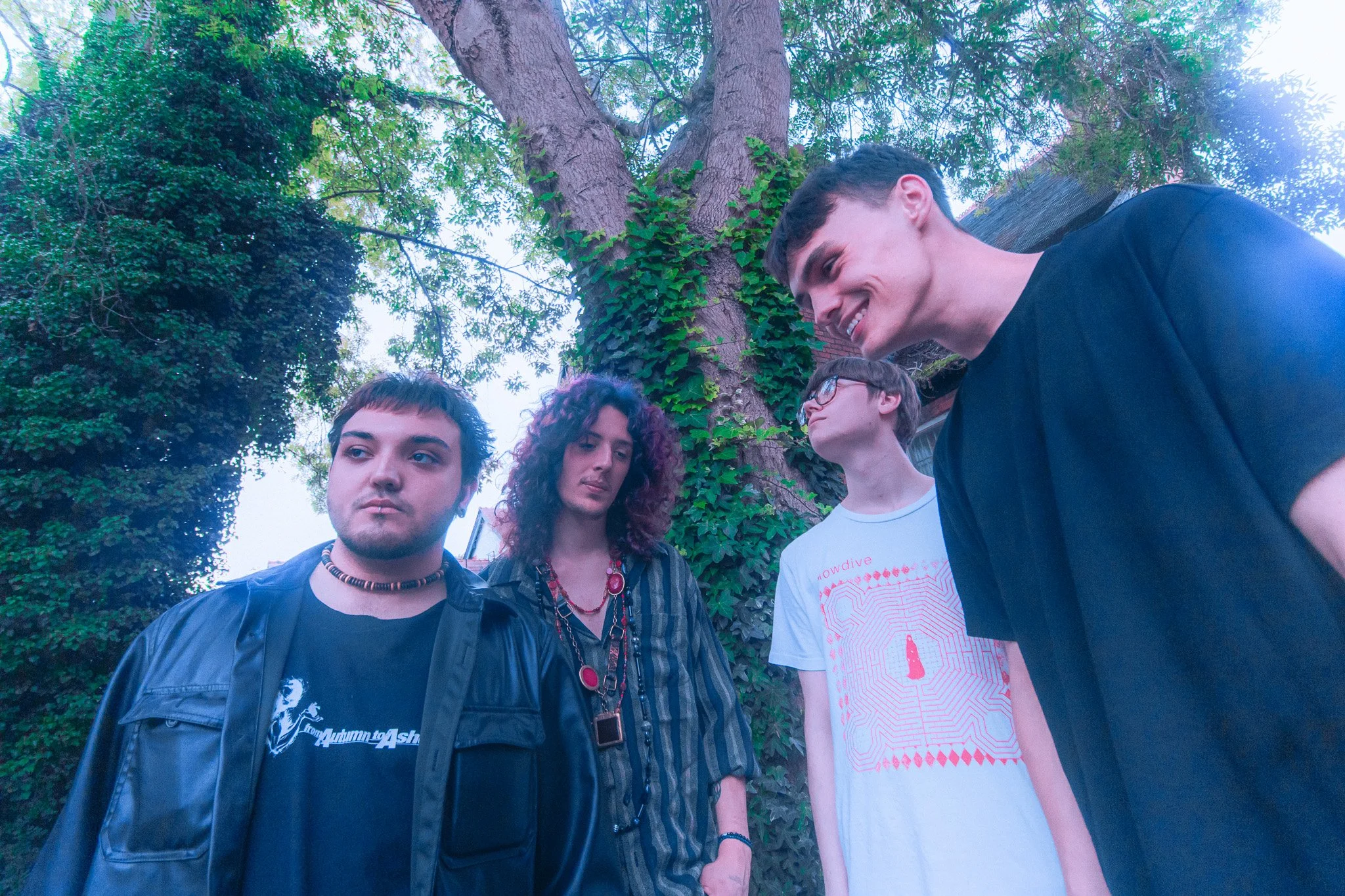 Our World's Collide at The Dark Horse, Moseley, Birmingham. standing near a large tree outdoors, with greenery in the background, leaning in towards each other, some looking at the camera and others looking away.