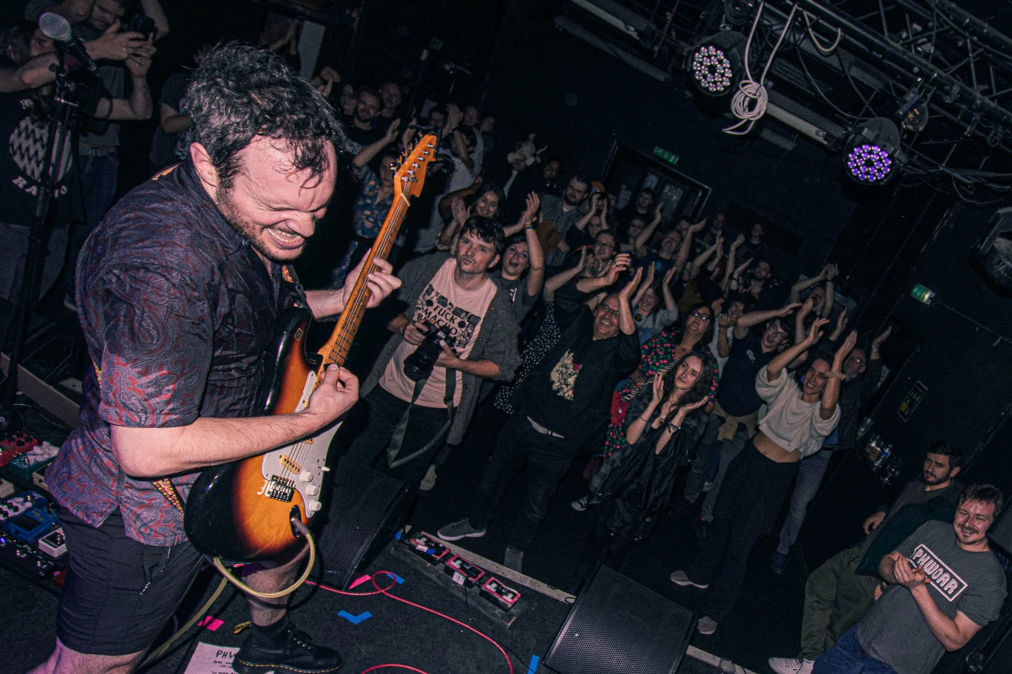 PHWOAR at Dead Wax, Digbeth, Birmingham. A guitarist playing on stage at a concert with an eager audience clapping and cheering.