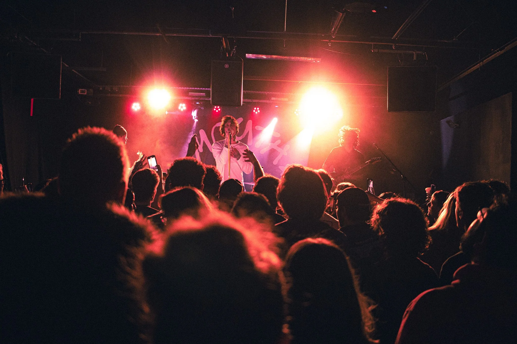 Mouth Culture. Devil's Dog, Digbeth, Birmingham. Crowd shot with vibrant red and yellow lighting. The lead singer is in the center holding a microphone, with a guitarist to their right. The audience is watching, some are taking photos.