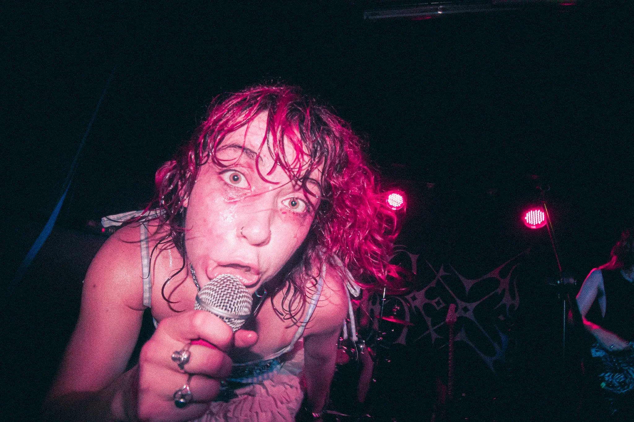 Bex at The Sunflower Lounge, Birmingham. Close-up of a female singer with pink curly hair holding a microphone, performing on stage with pink and purple lighting.