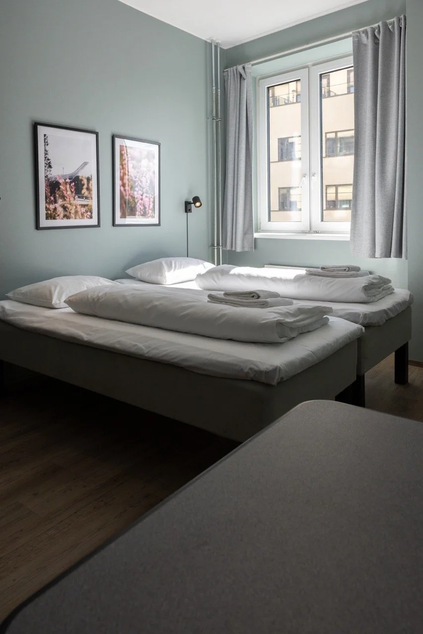 Practical private room with double bed and a small kitchenette area with plates and dishes, and an open clothing rack in the background. Affordable hostel in central Oslo. Stay in trendy Grünerløkka when you visit Oslo