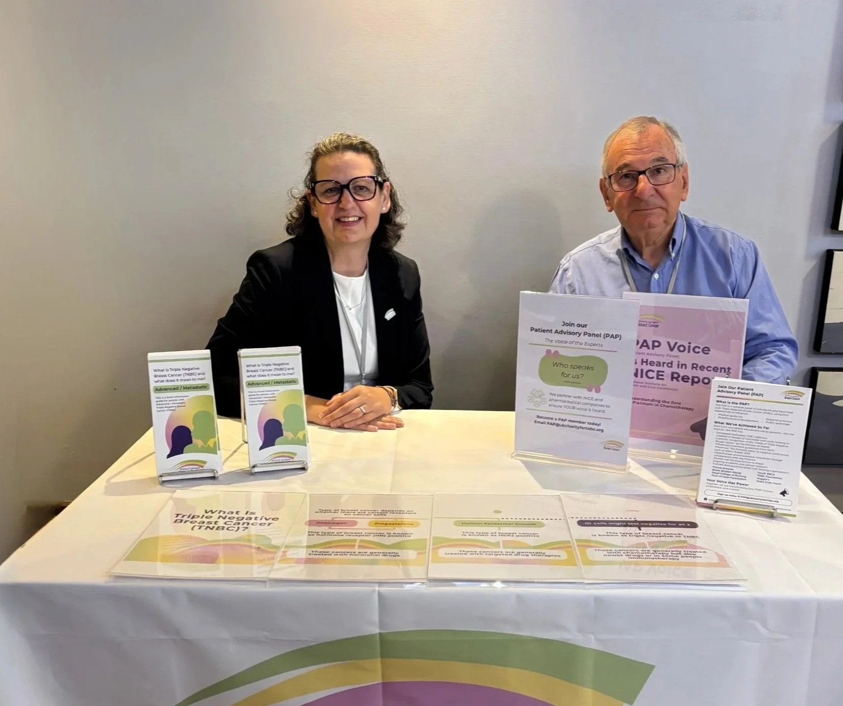 An image of smiling charity workers presenting leaflets and information about TNBC and the Patient Advisory Panel.