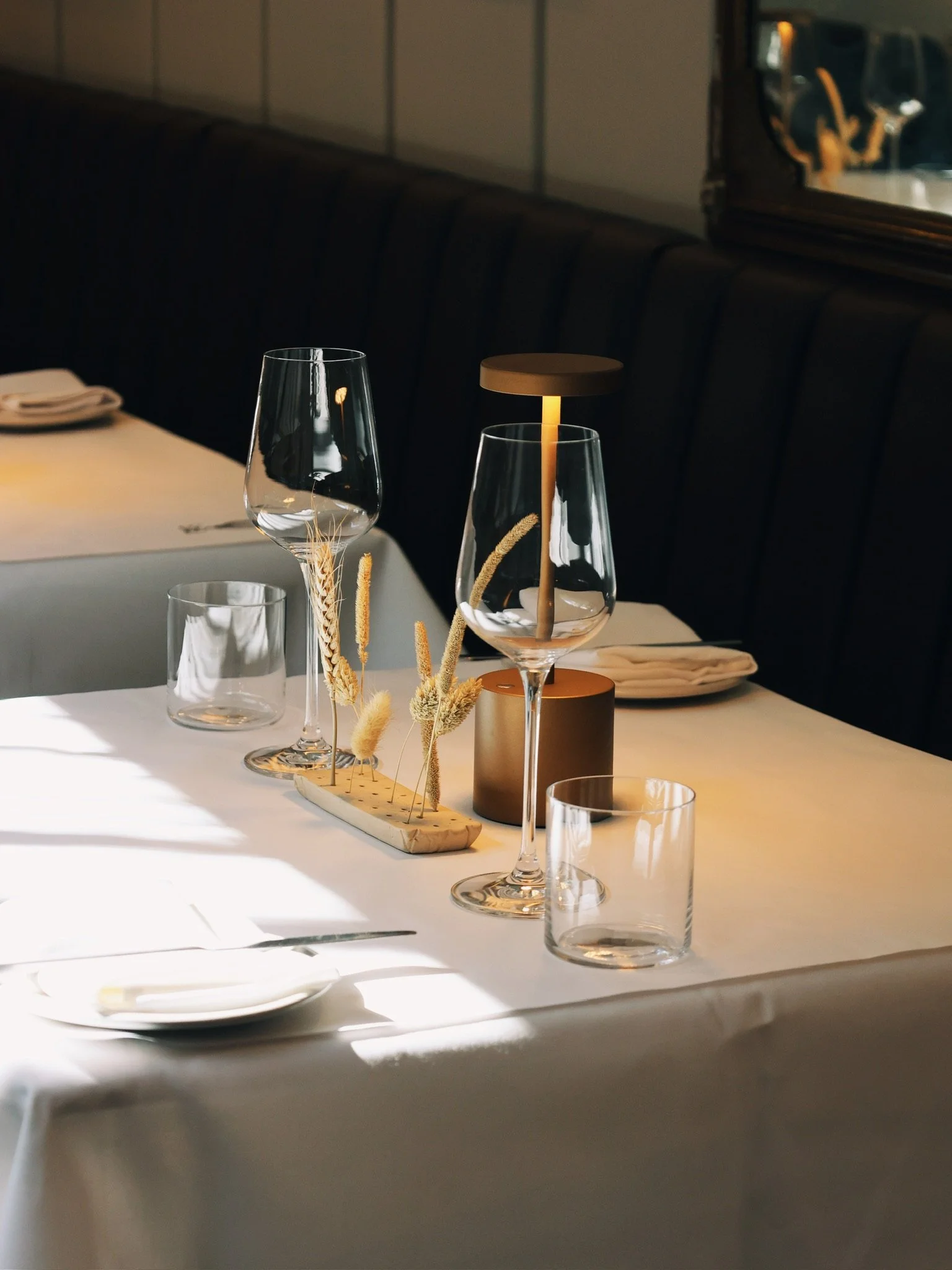 Elegant dining table setup with wine glasses, a modern candle holder, and dried floral decor, illuminated by soft natural light.