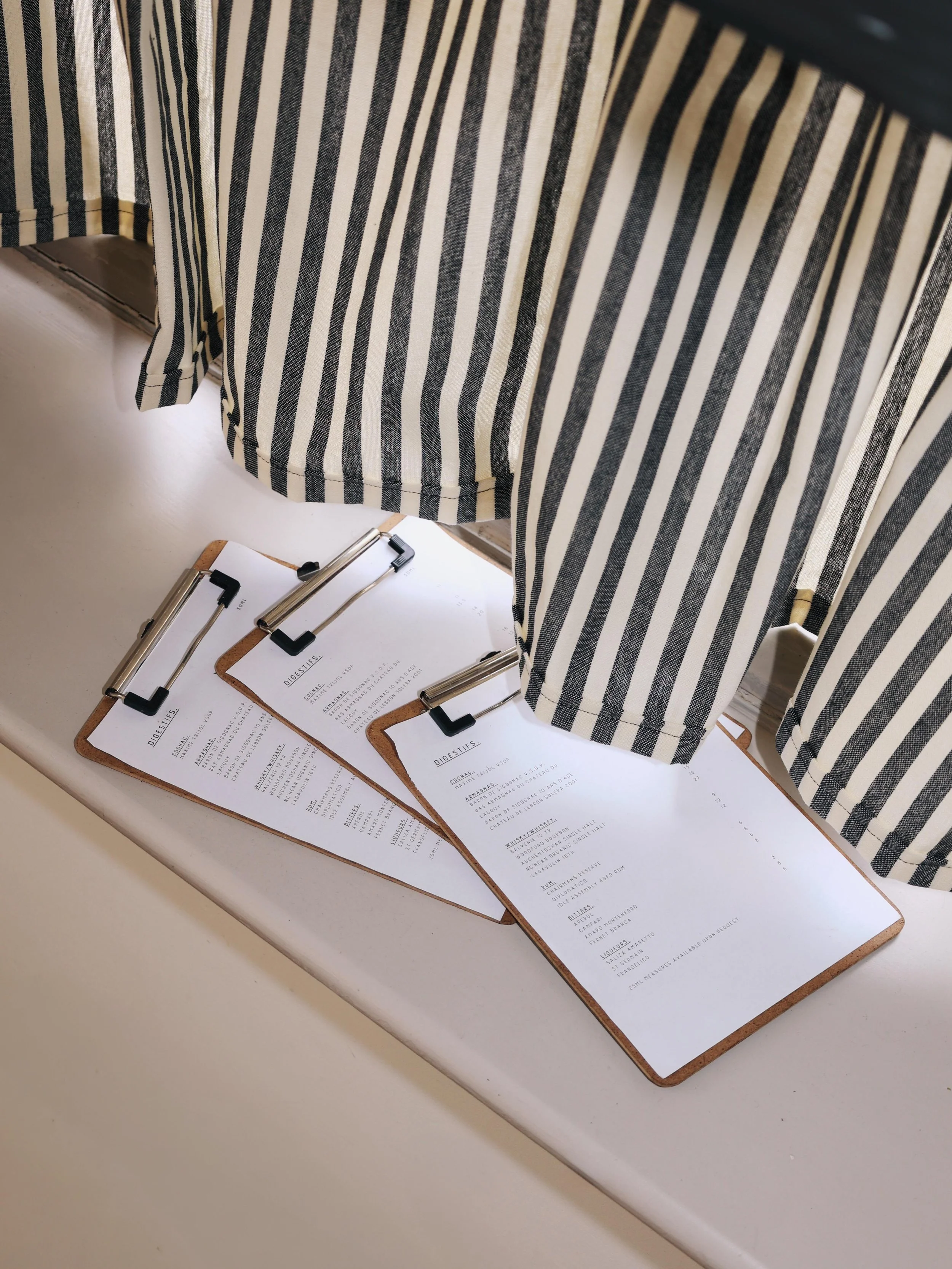 A restaurant table with three clipboards holding menus, with a striped curtain hanging above.