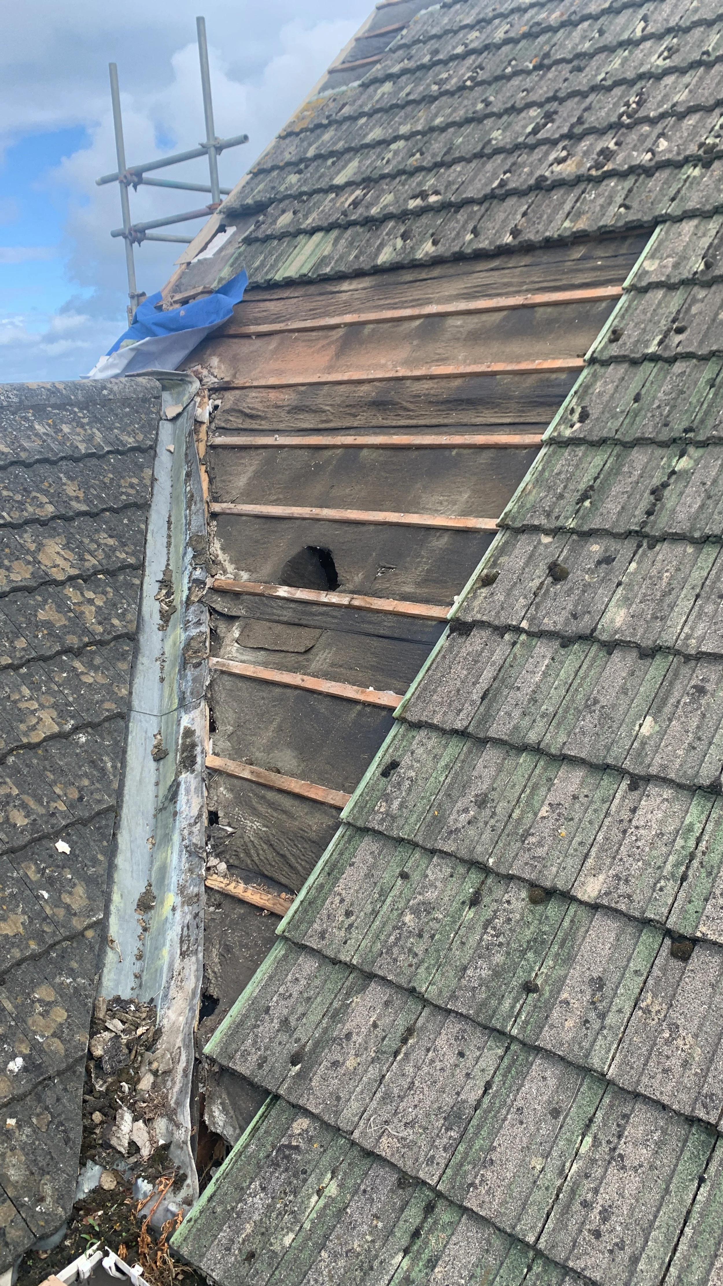 Roof with missing and damaged shingles, showing the underlying wooden structure during repair.