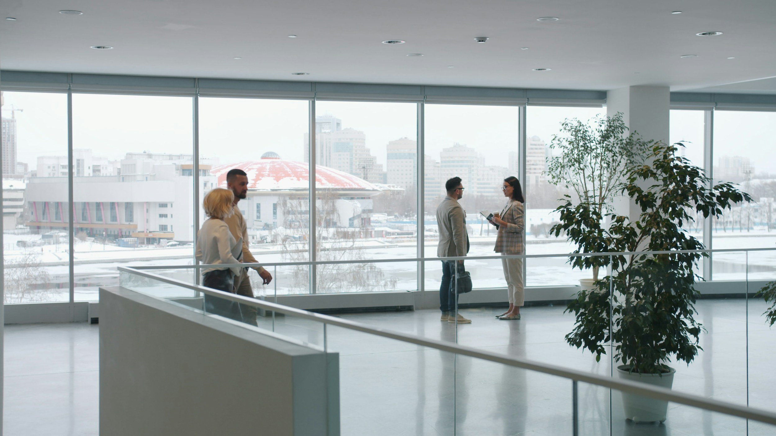 Four people talking in a bright office with large windows and a snowy city view outside.