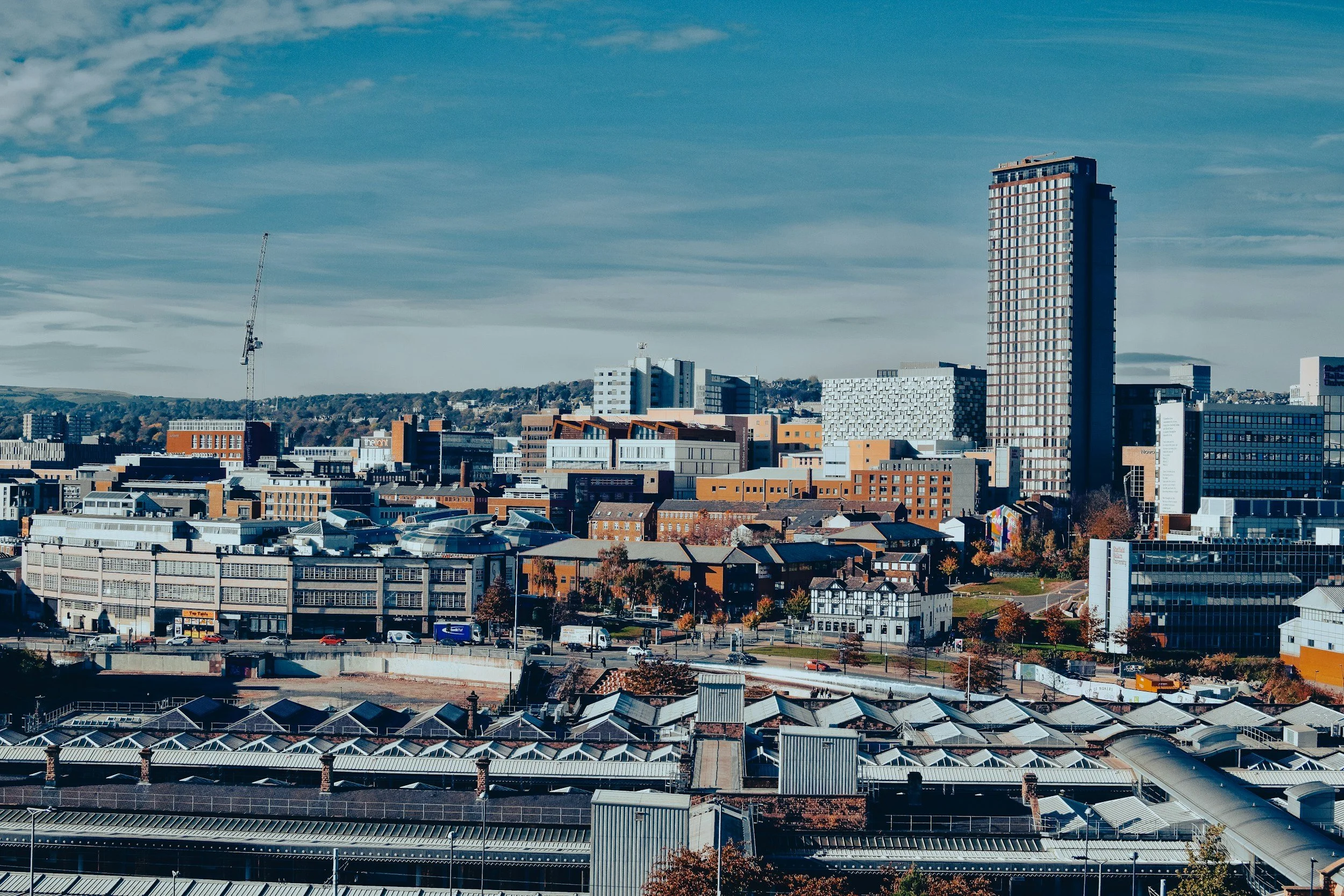Sheffield skyline with various buildings, a tall high-rise, a construction crane, and a mix of commercial and residential structures under a partly cloudy sky.