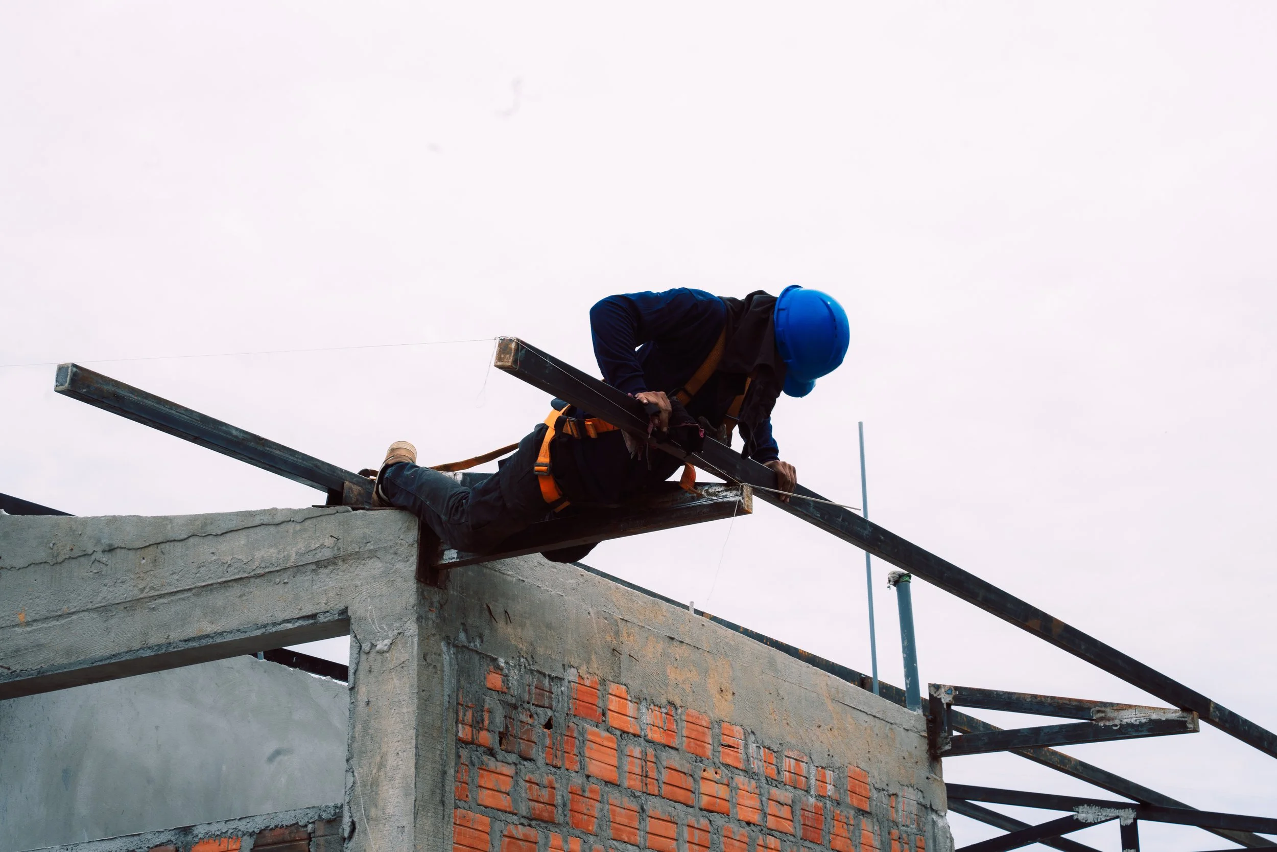Construction worker wearing a blue safety helmet and harness working on the edge of a building under construction with exposed brick and concrete walls.