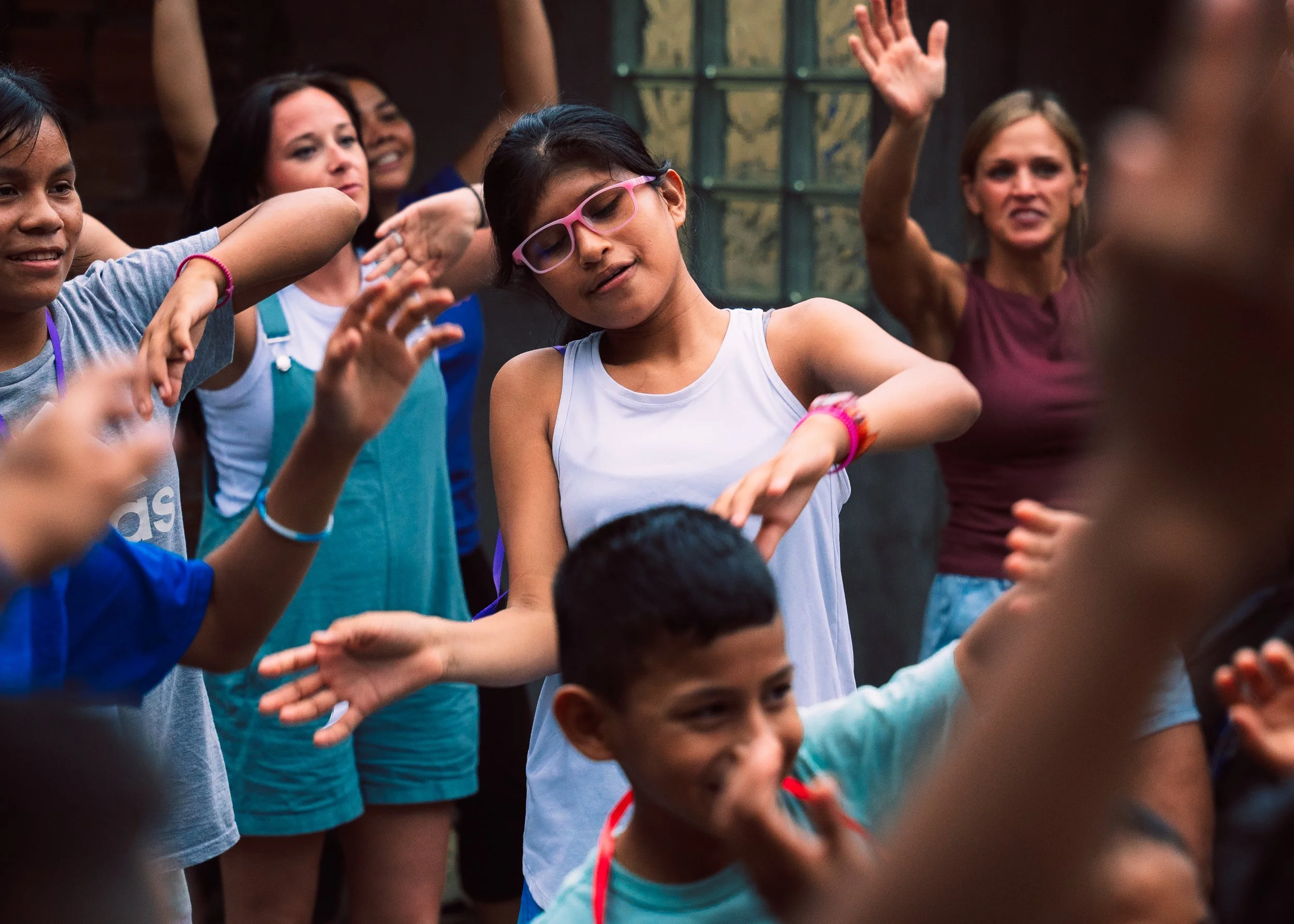 Group of children dancing together outdoors, joyfully engaging in a celebration or activity, with some raising their hands and smiling.