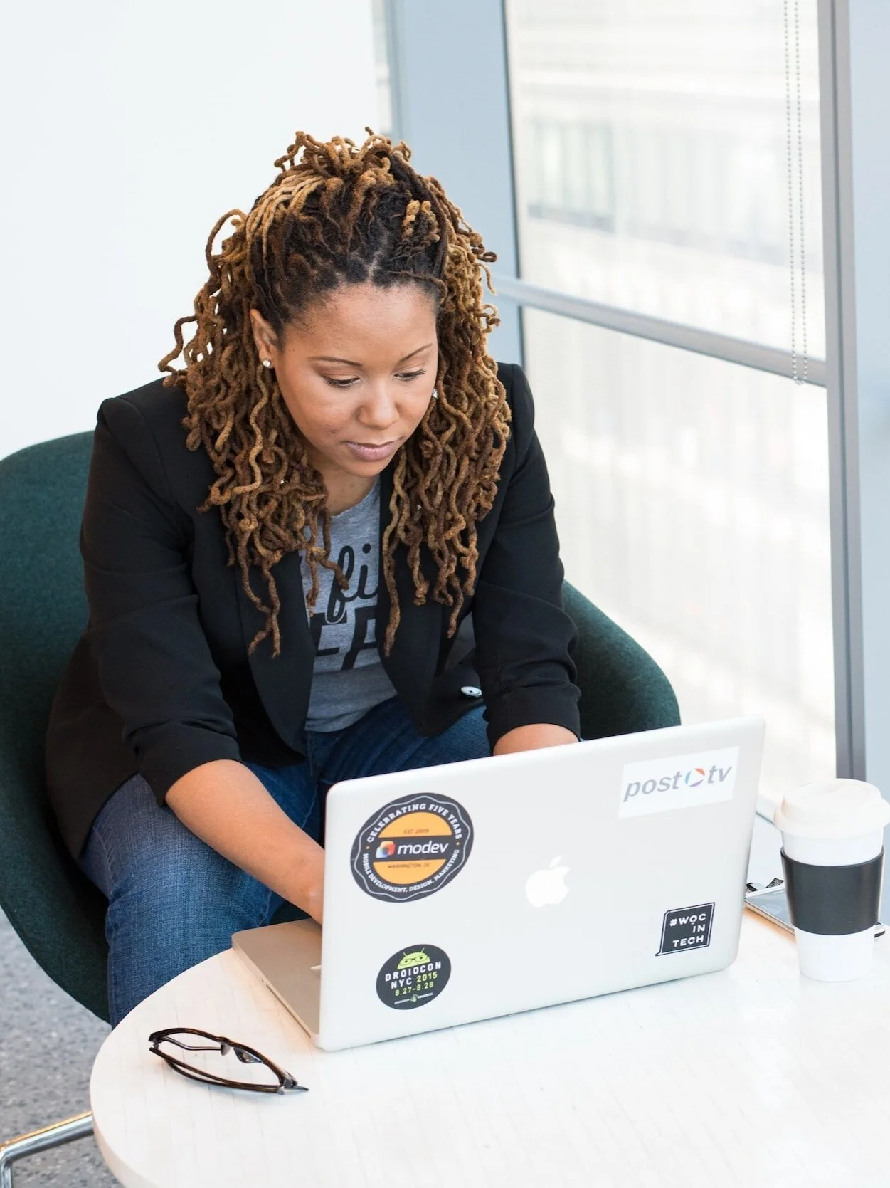 Woman sitting at coffee table near window working on laptop
