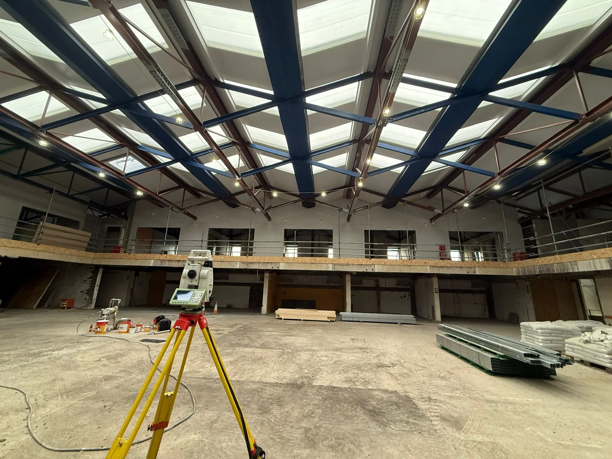 Construction site inside a large building with a blue and white vaulted ceiling, construction equipment, and building materials on the floor.