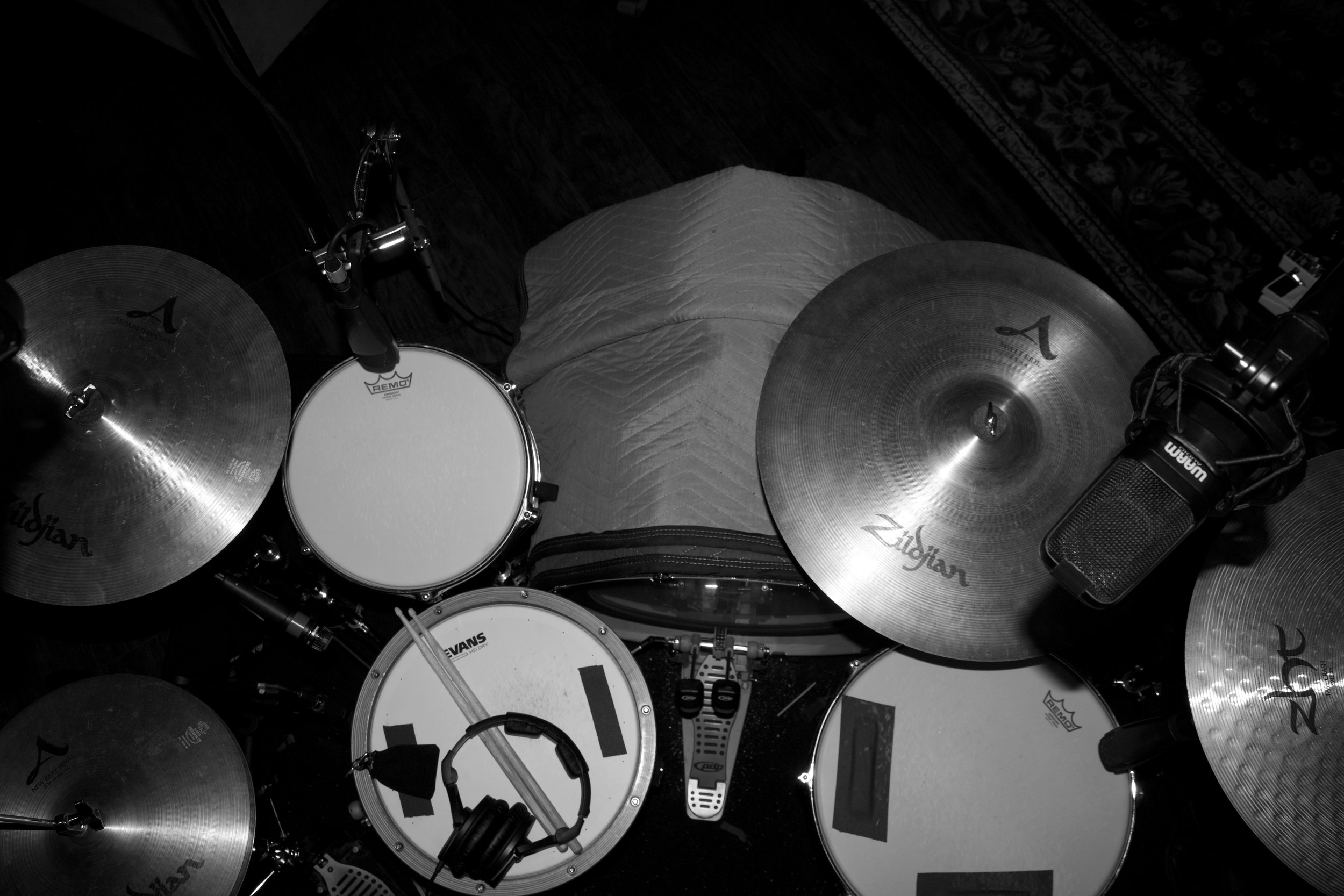 A top-down view of a drum set with a snare with wooden hoops, rack tom, floor tom, kick drum, hi hat, ride cymbal, and two crash cymbals, with various microphones.