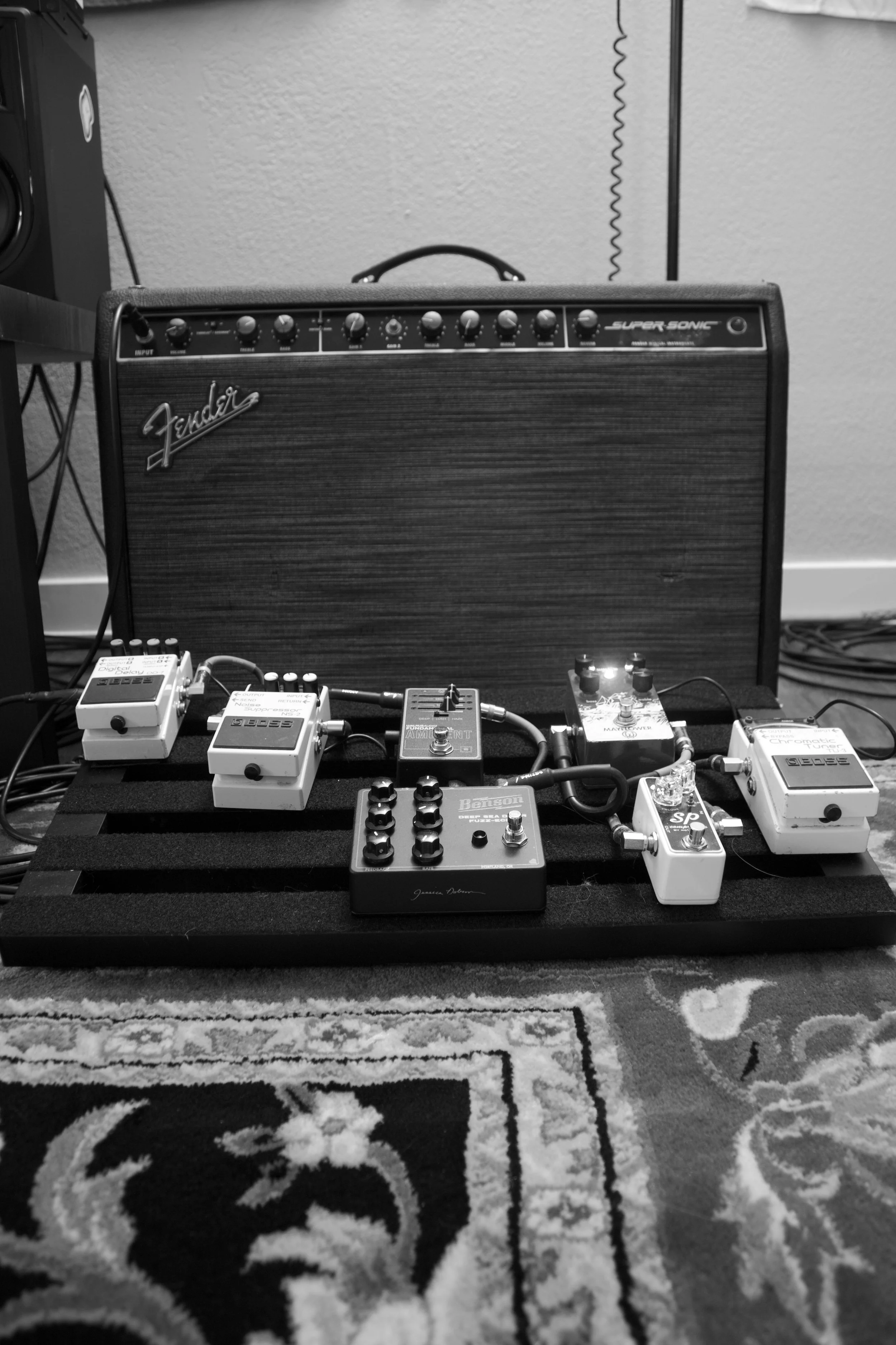 A guitar combo amplifier with a pedalboard in front of it, full of guitar pedals.