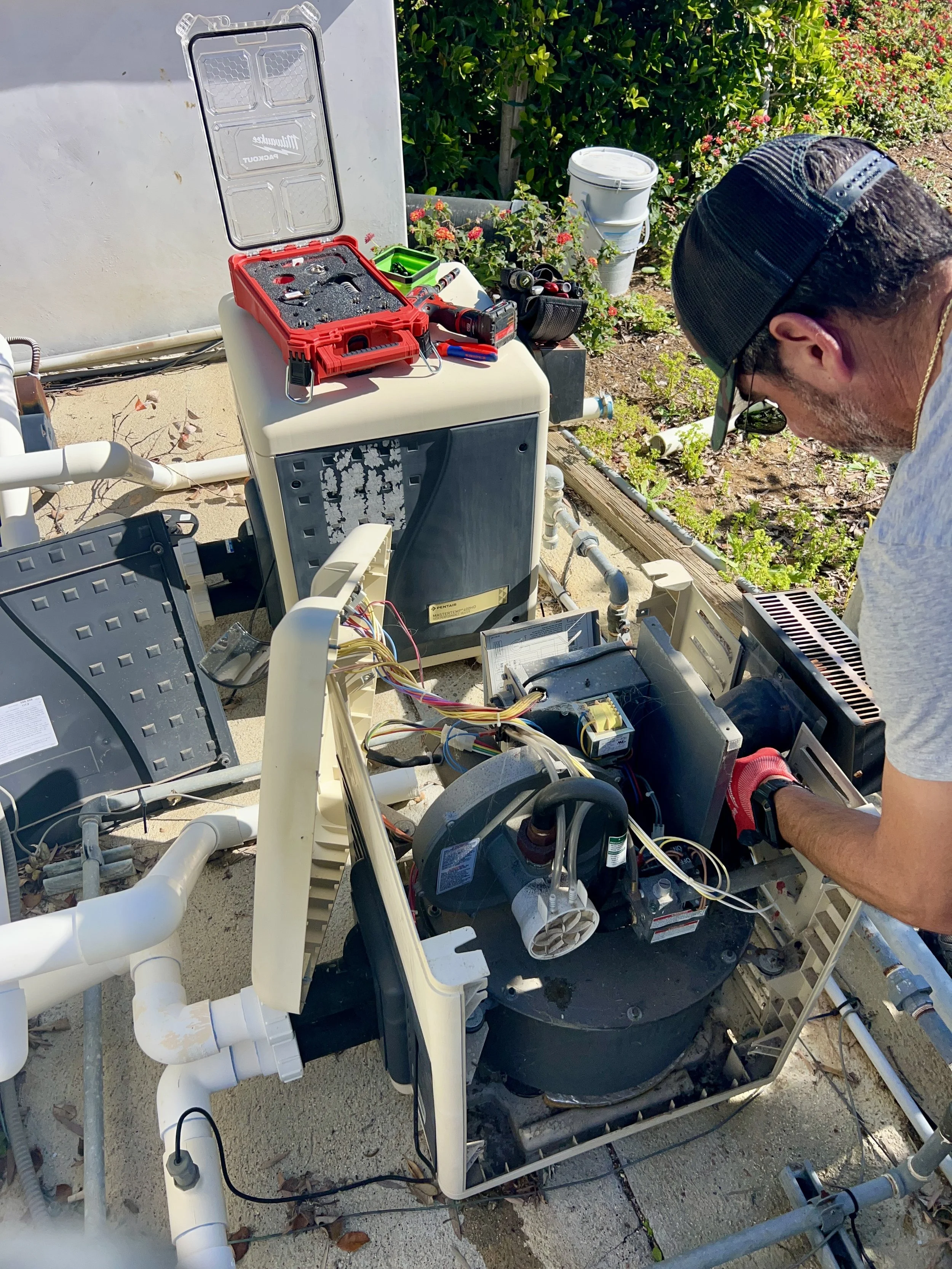Technician repairing or working on a water treatment or filtration system outside, with pipes and electronic components visible.
