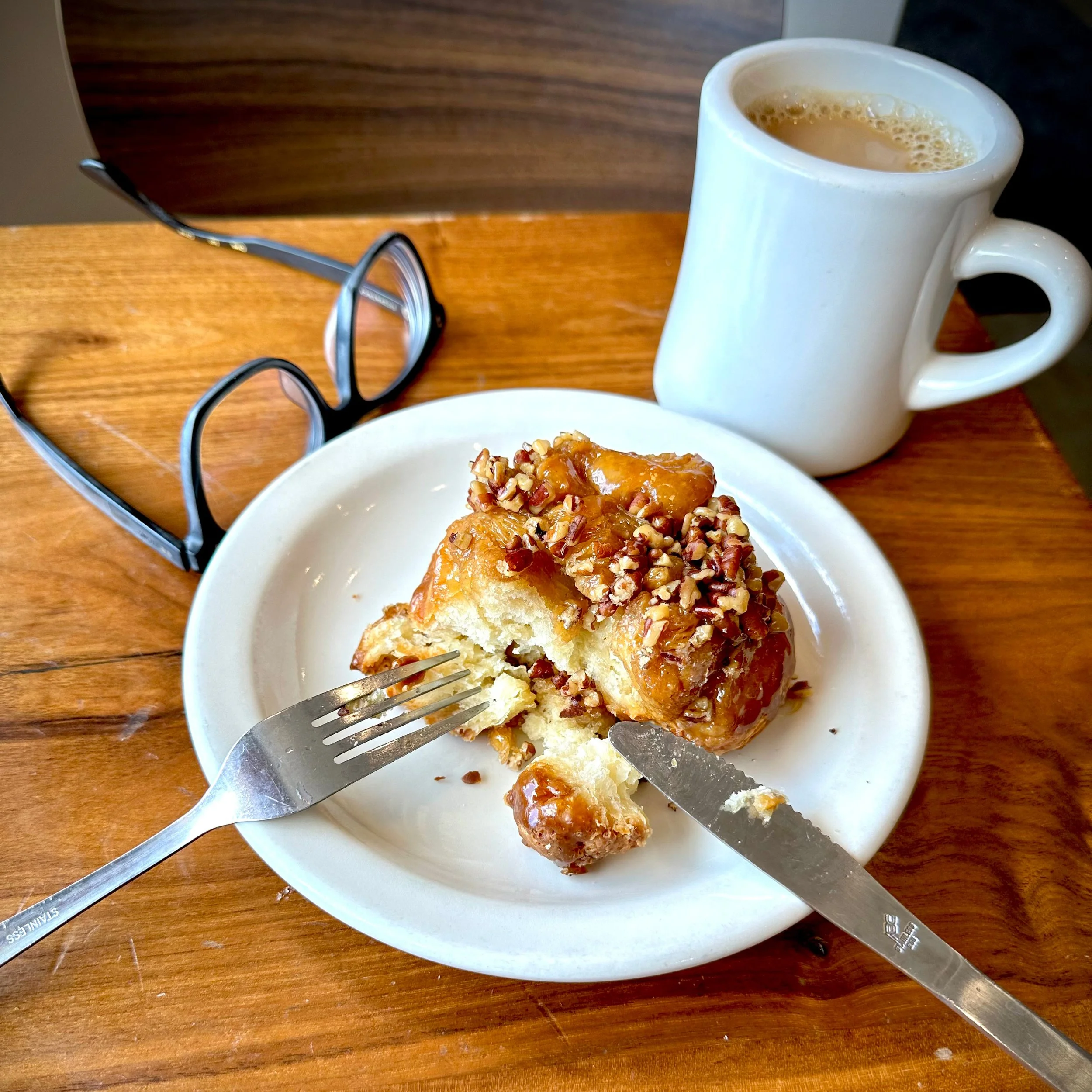 Photo of a table setting, with a partially eaten pastry, a pair of glasses, and a cup of coffee.