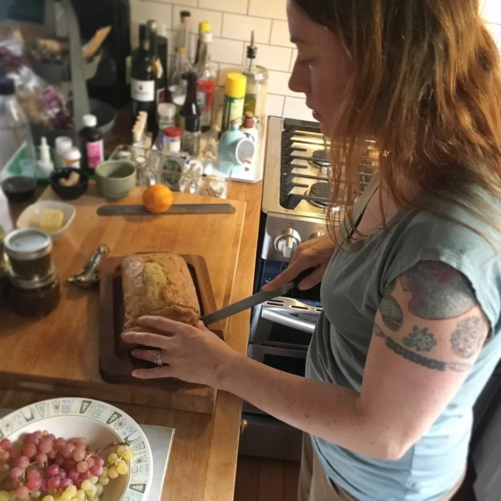 Photograph of food writer and historian Heather Arndt-Anderson in her home kitchen, slicing a piece of loaf cake.
