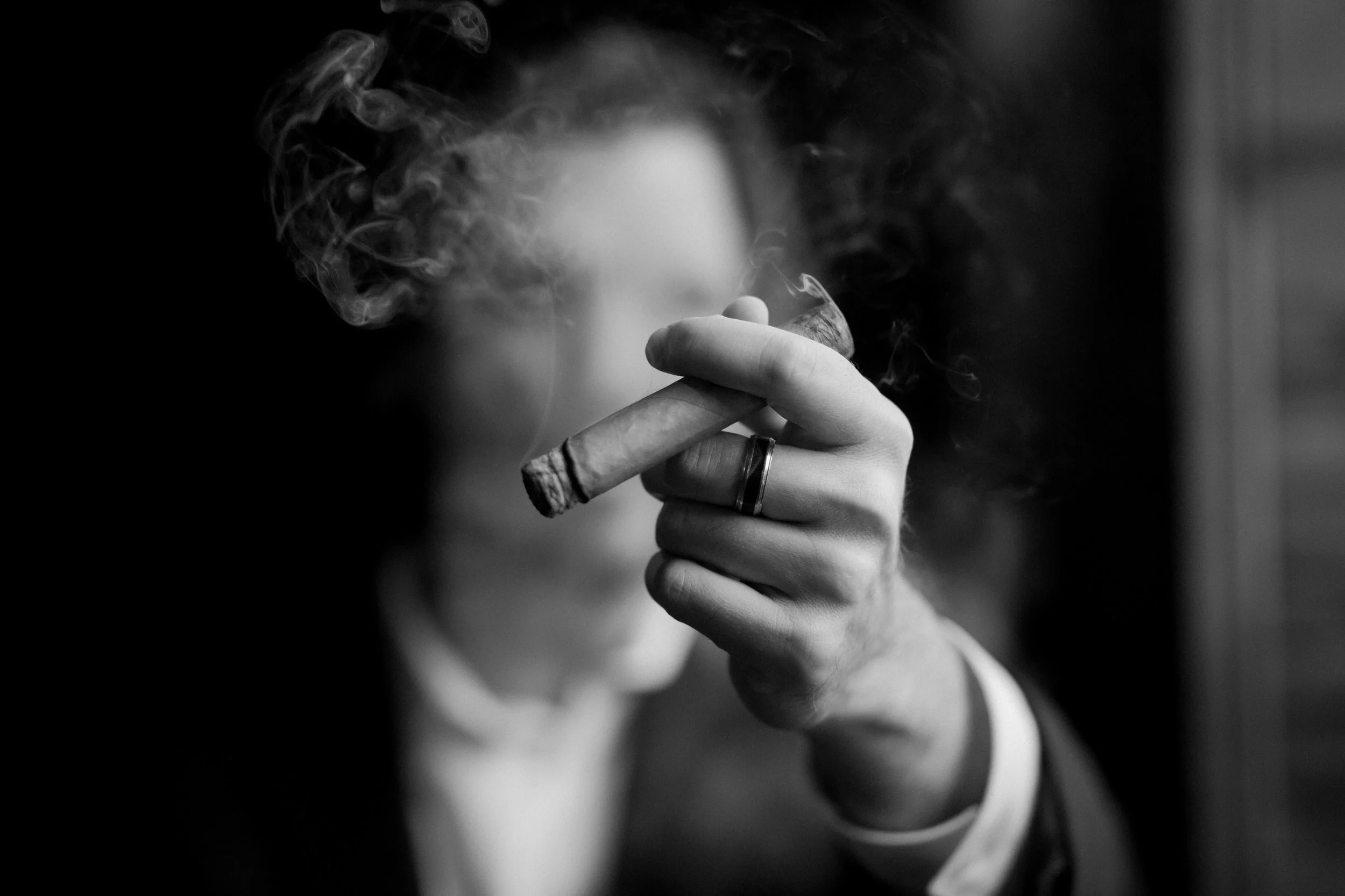 Man holding a cigar surrounded by smoke — symbolizing reflection, time, and presence in Blue Bay Fund’s essay on why people smoke cigars.