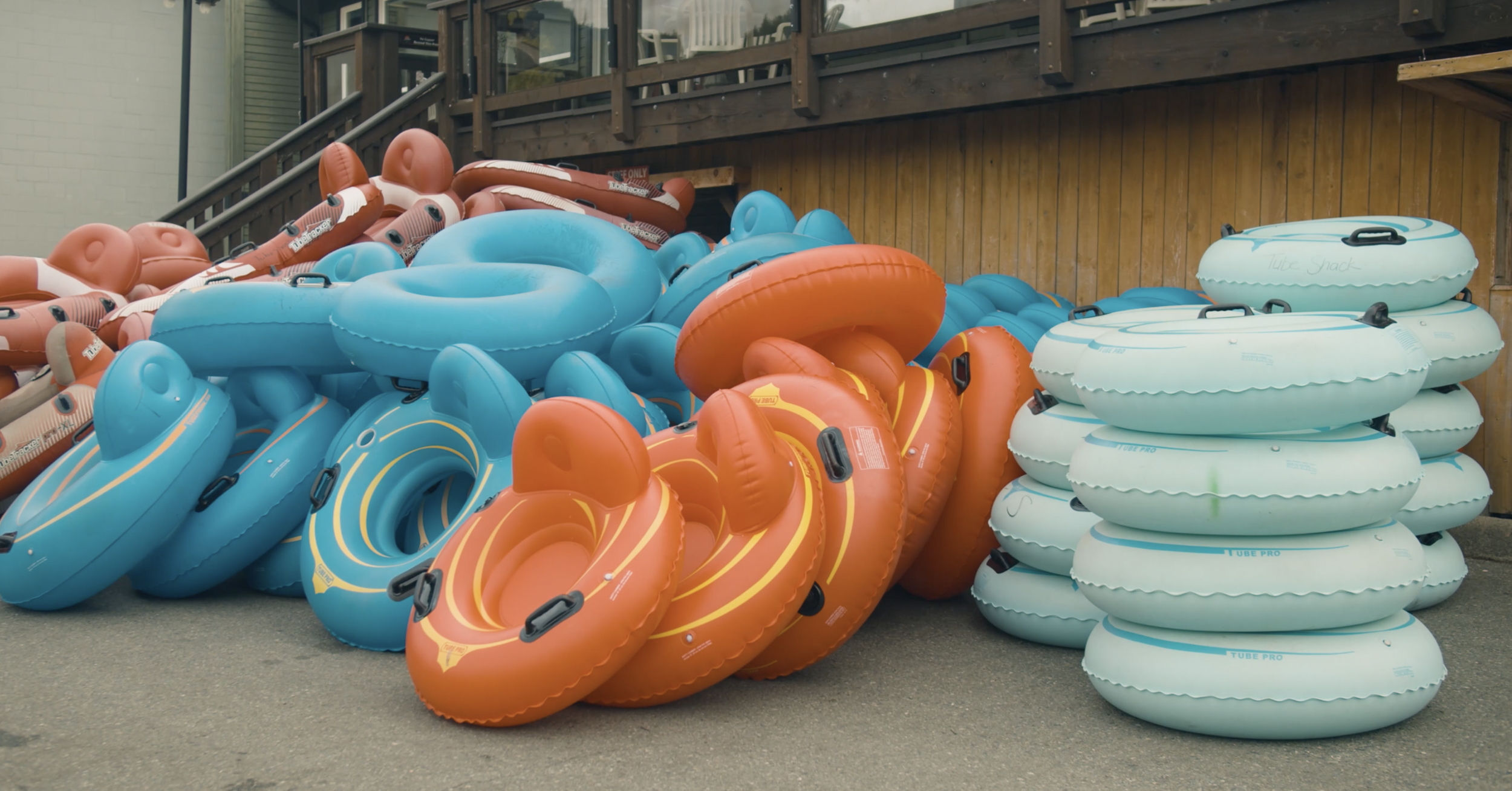 Stacks of colorful inflatable inner tubes in blue, red, and teal, arranged outside near a wooden building.