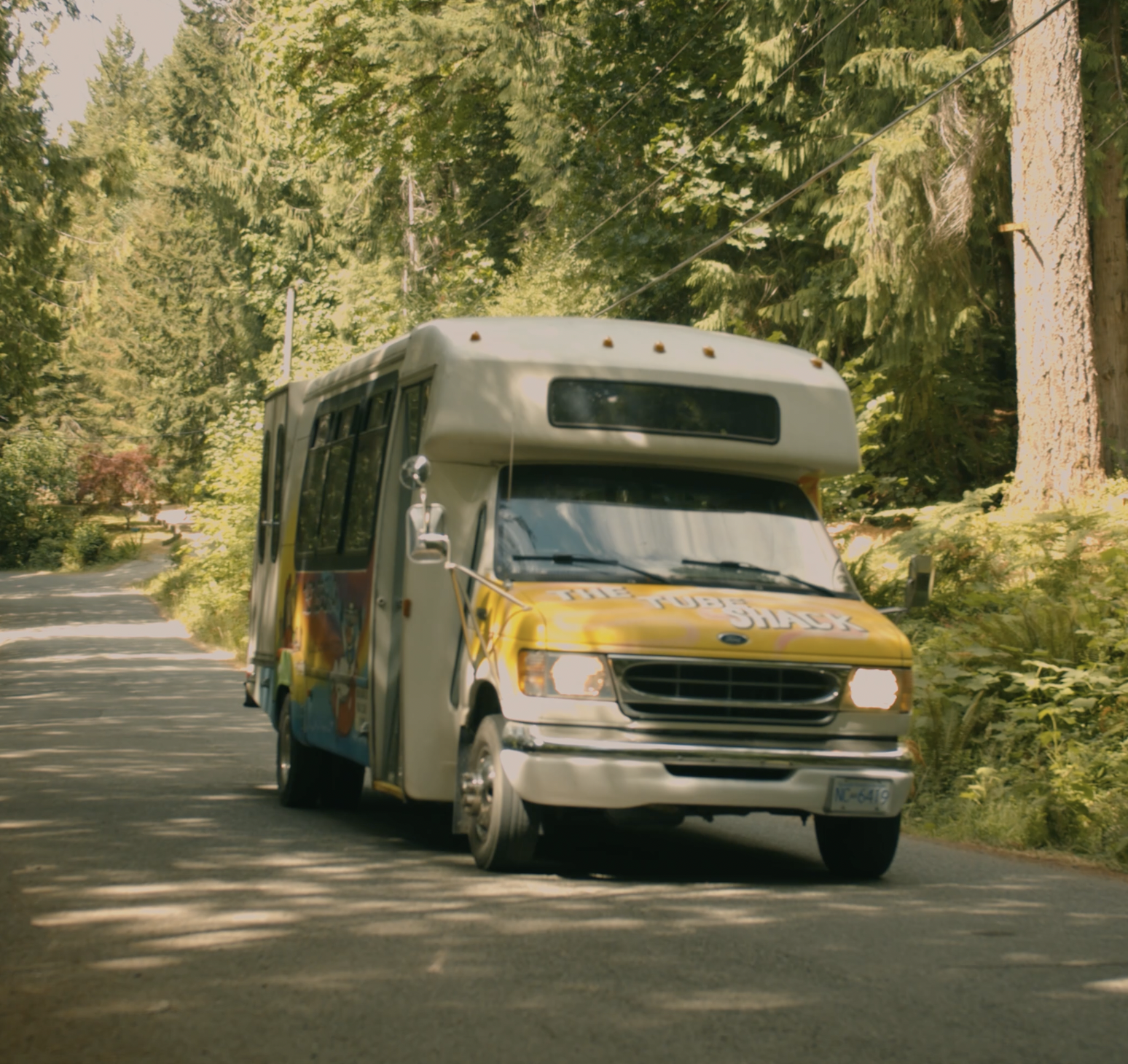 A colourful Tube Shack shuttle driving down a shaded wooded road.