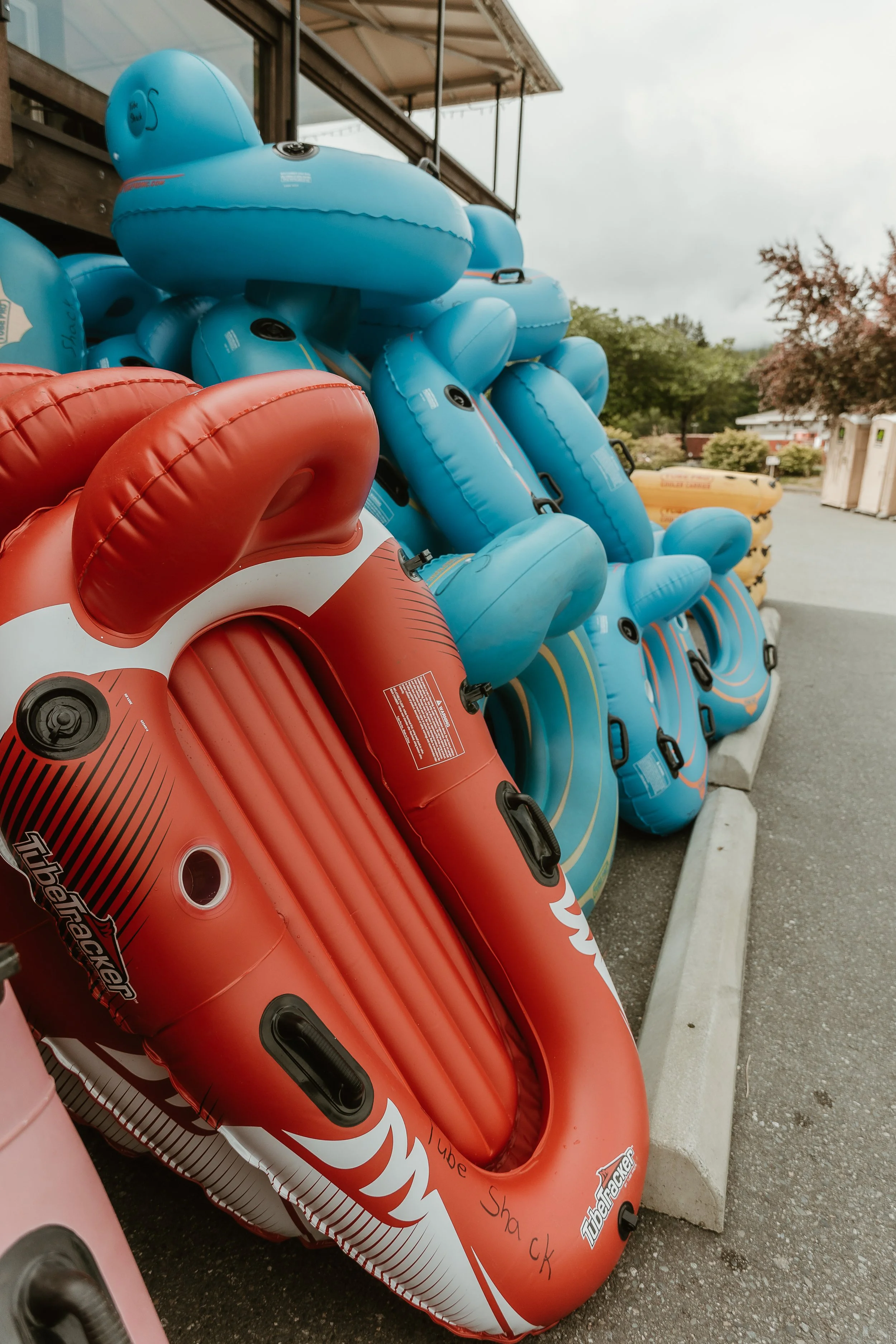 Stacked inflatable pool floats in blue and red outside of the Tube Shack, with trees and a cloudy sky in the background.