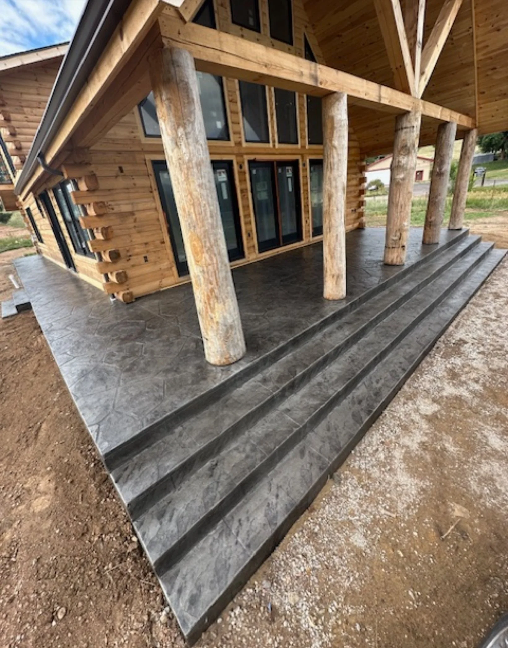 A wooden house with a stone porch and steps, supported by large logs, during daytime.