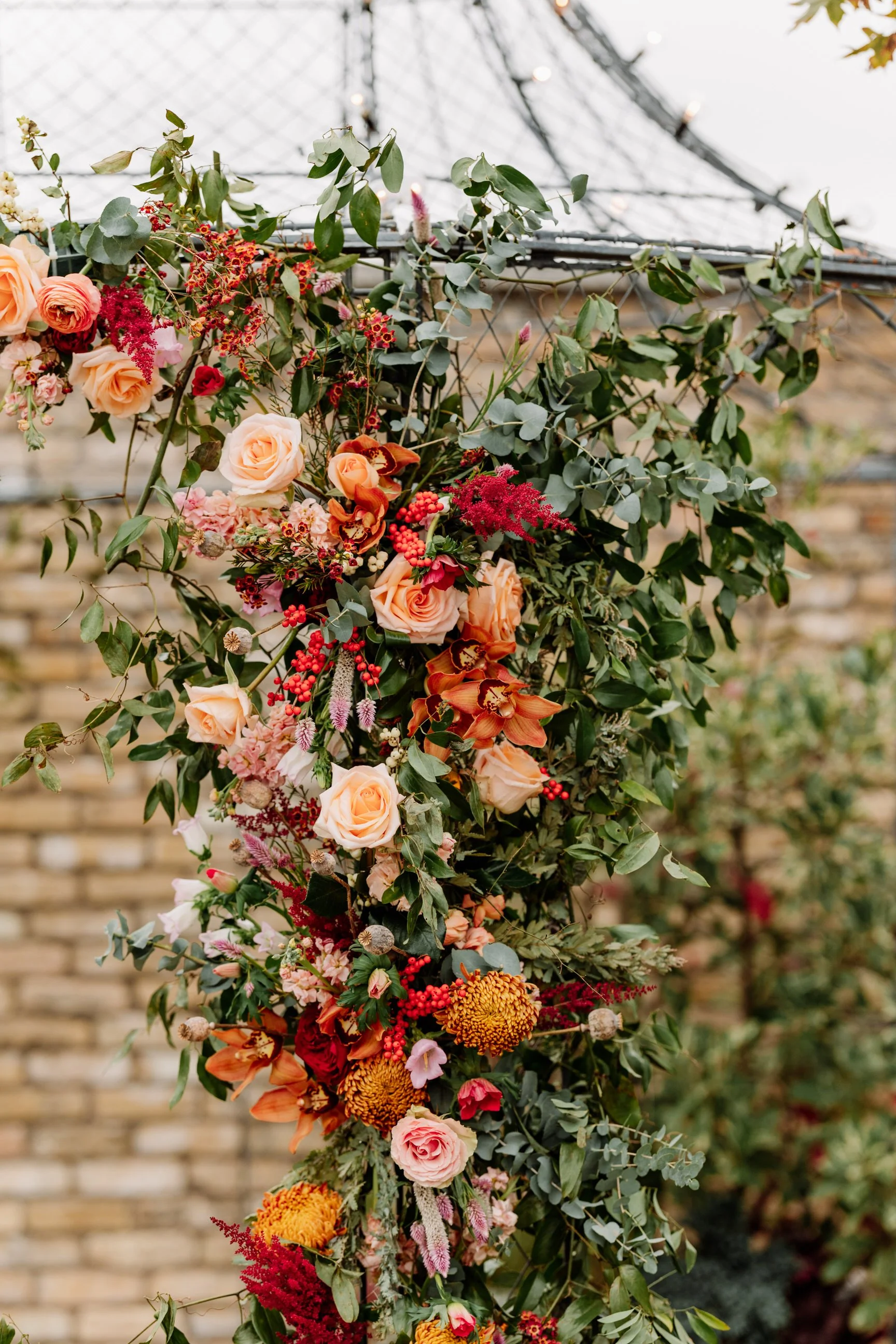 A floral arrangement with roses, orchids, and other flowers on a trellis outdoors.