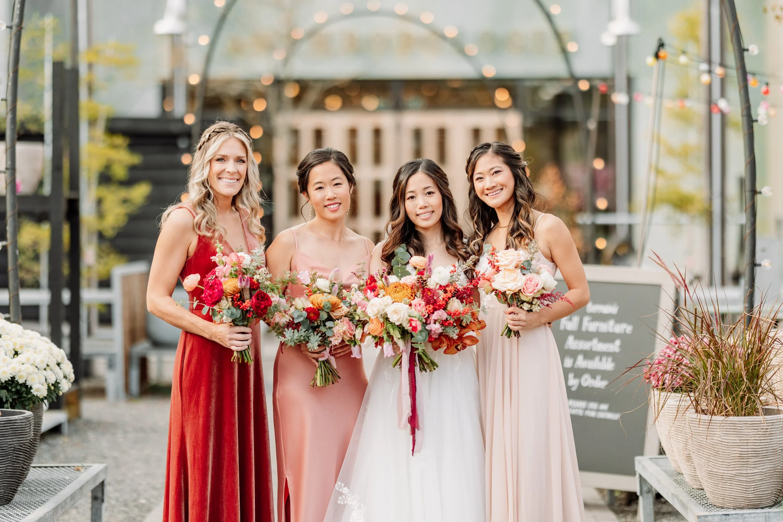 Four women in formal dresses holding bouquets of flowers at a wedding reception.