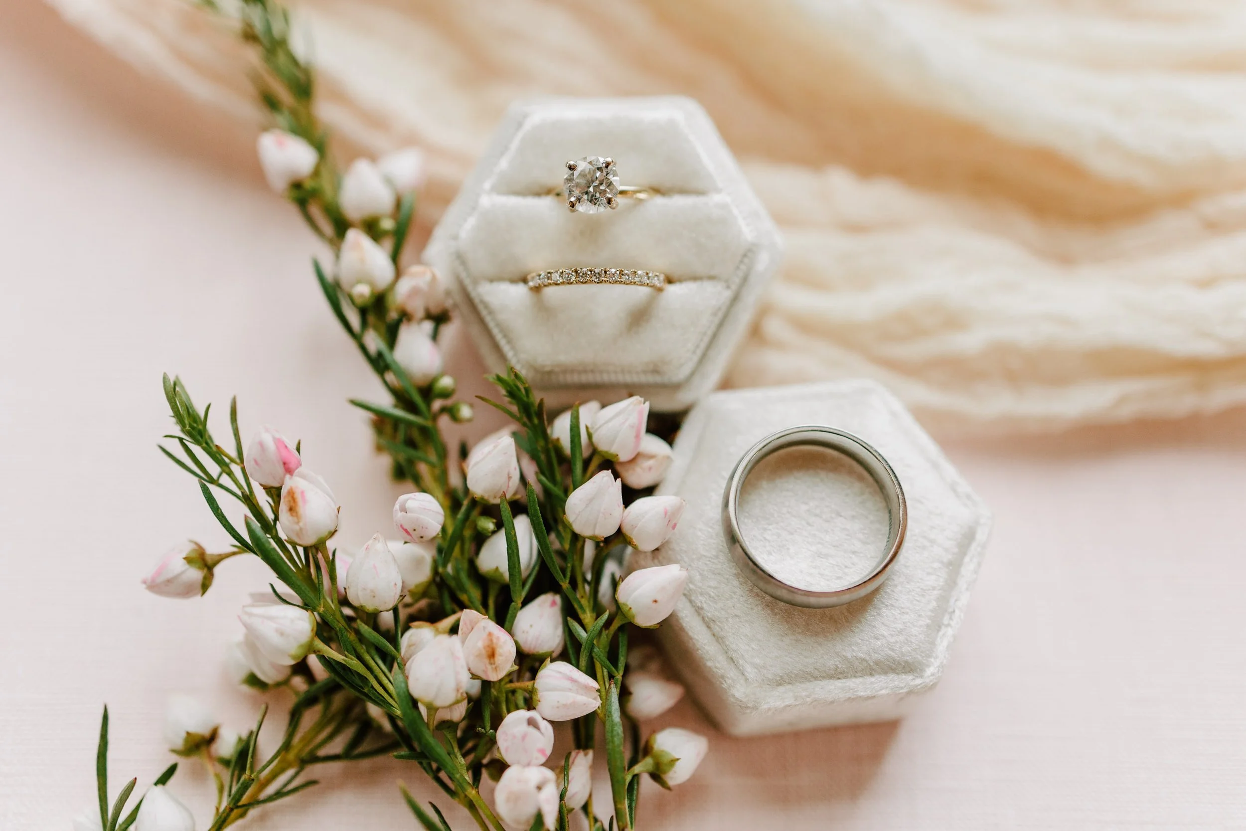 Wedding rings on velvet hexagon boxes with pink and white flowers and greenery.