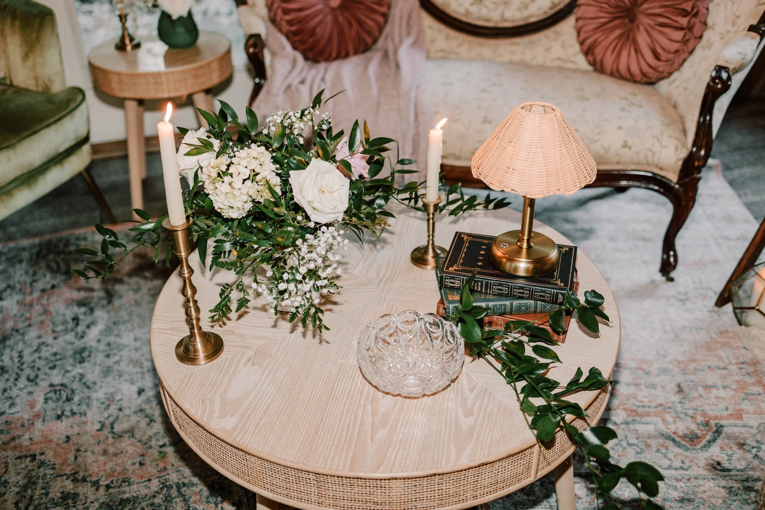 Decorative living room table with candles, floral arrangement, books, and a table lamp.