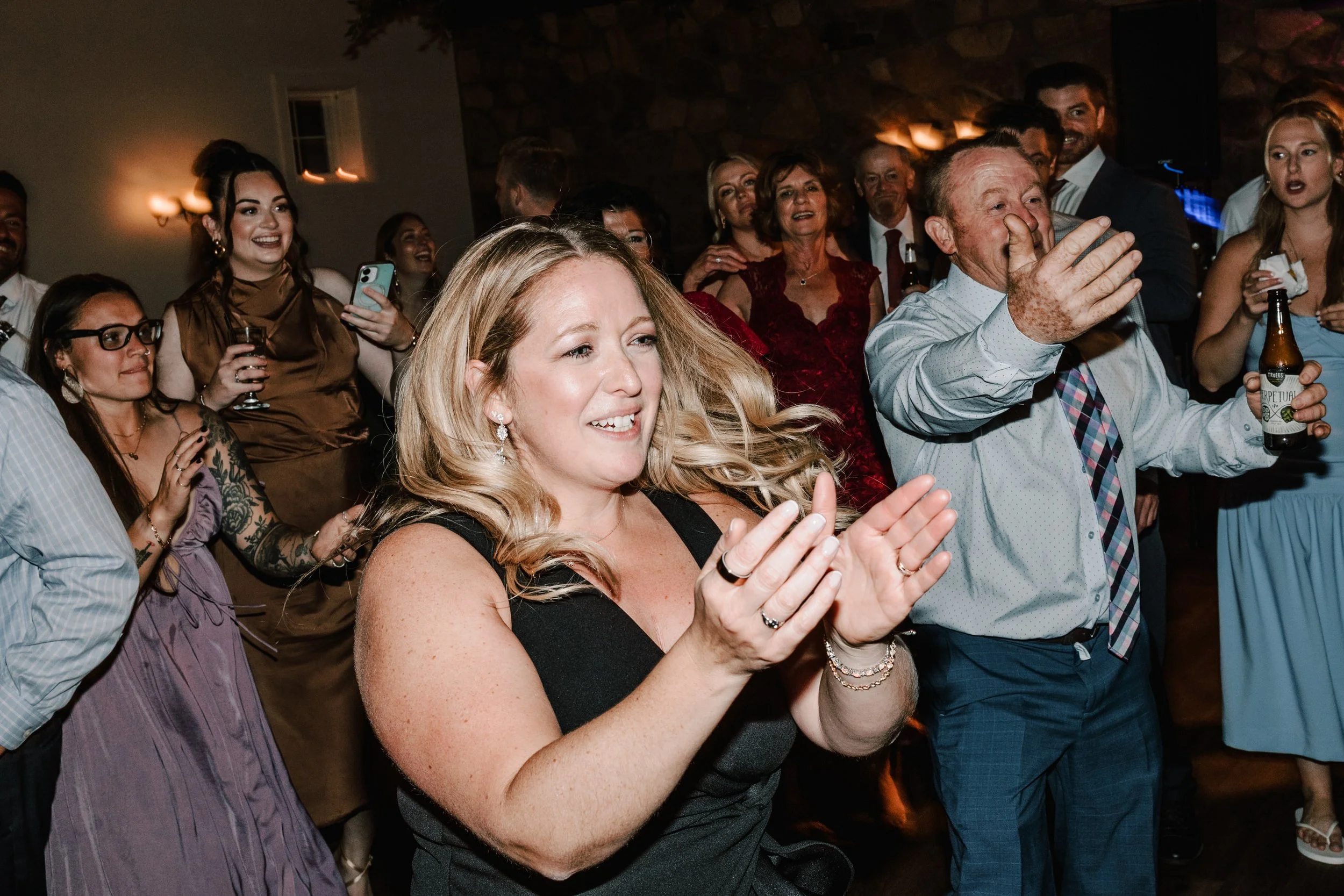 People at a celebration dancing and cheering, some clapping and holding drinks, with everyone smiling and enjoying the moment.