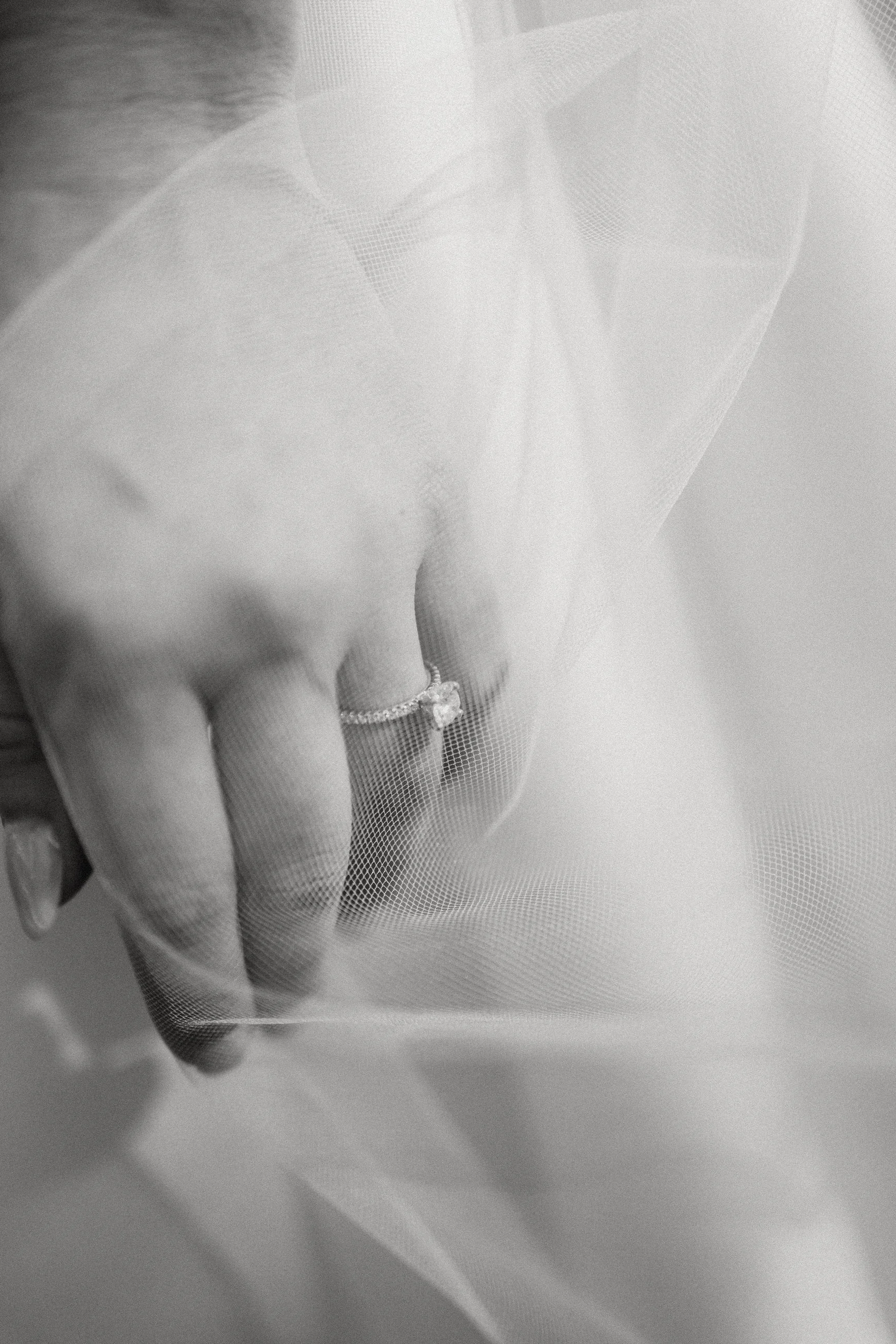 Close-up of a bride's hand wearing a ring, gently touching her wedding dress or veil, with soft focus and delicate fabric