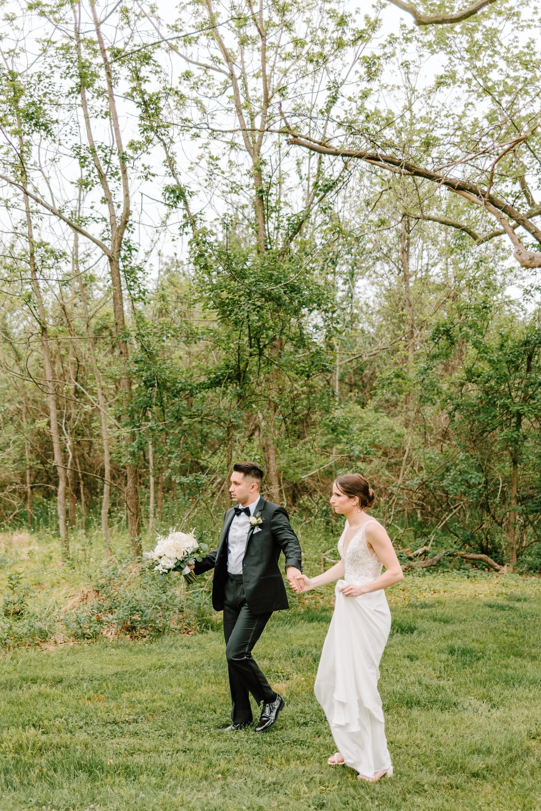 Bride and groom holding hands walking on grass in a wooded outdoor setting