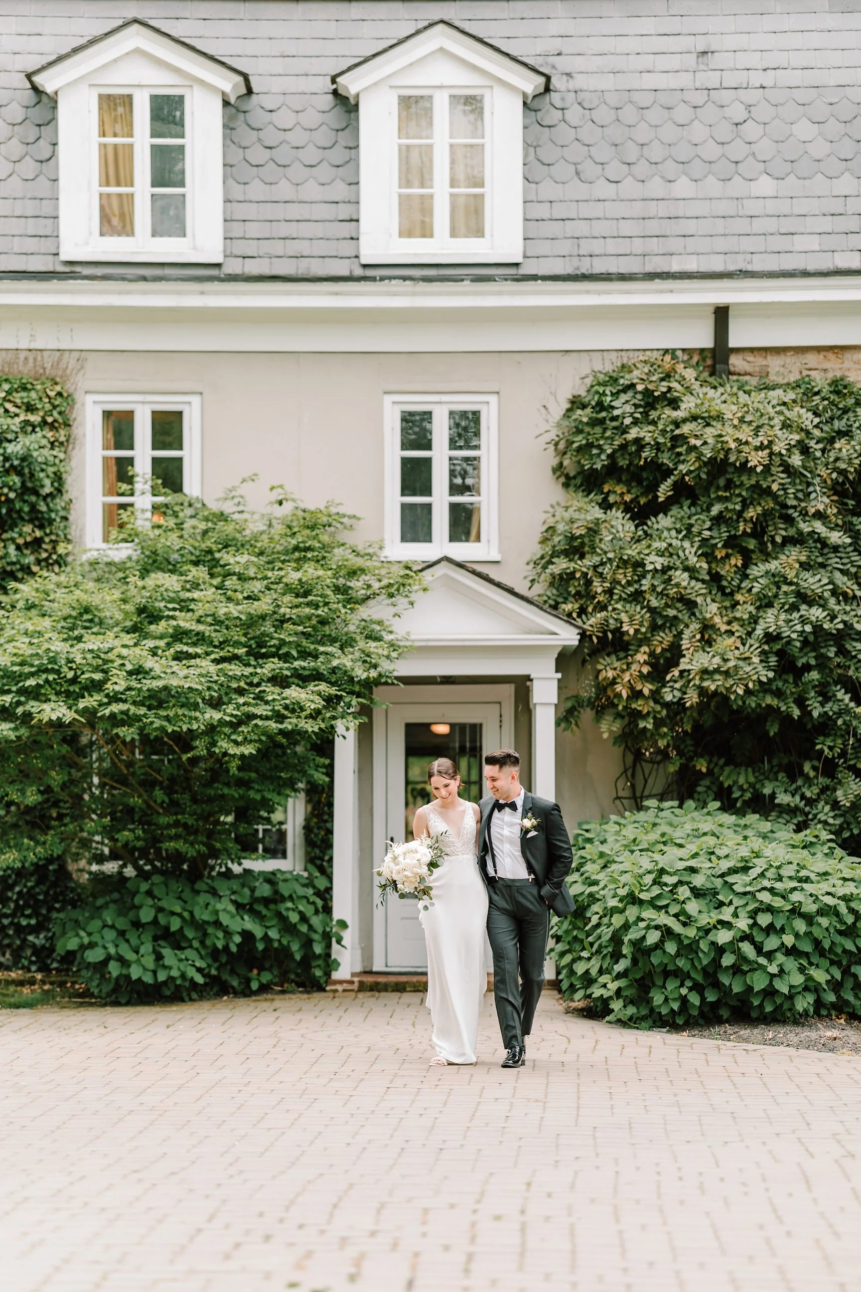 Bride and groom walking out of a house, the bride holding a bouquet of flowers.