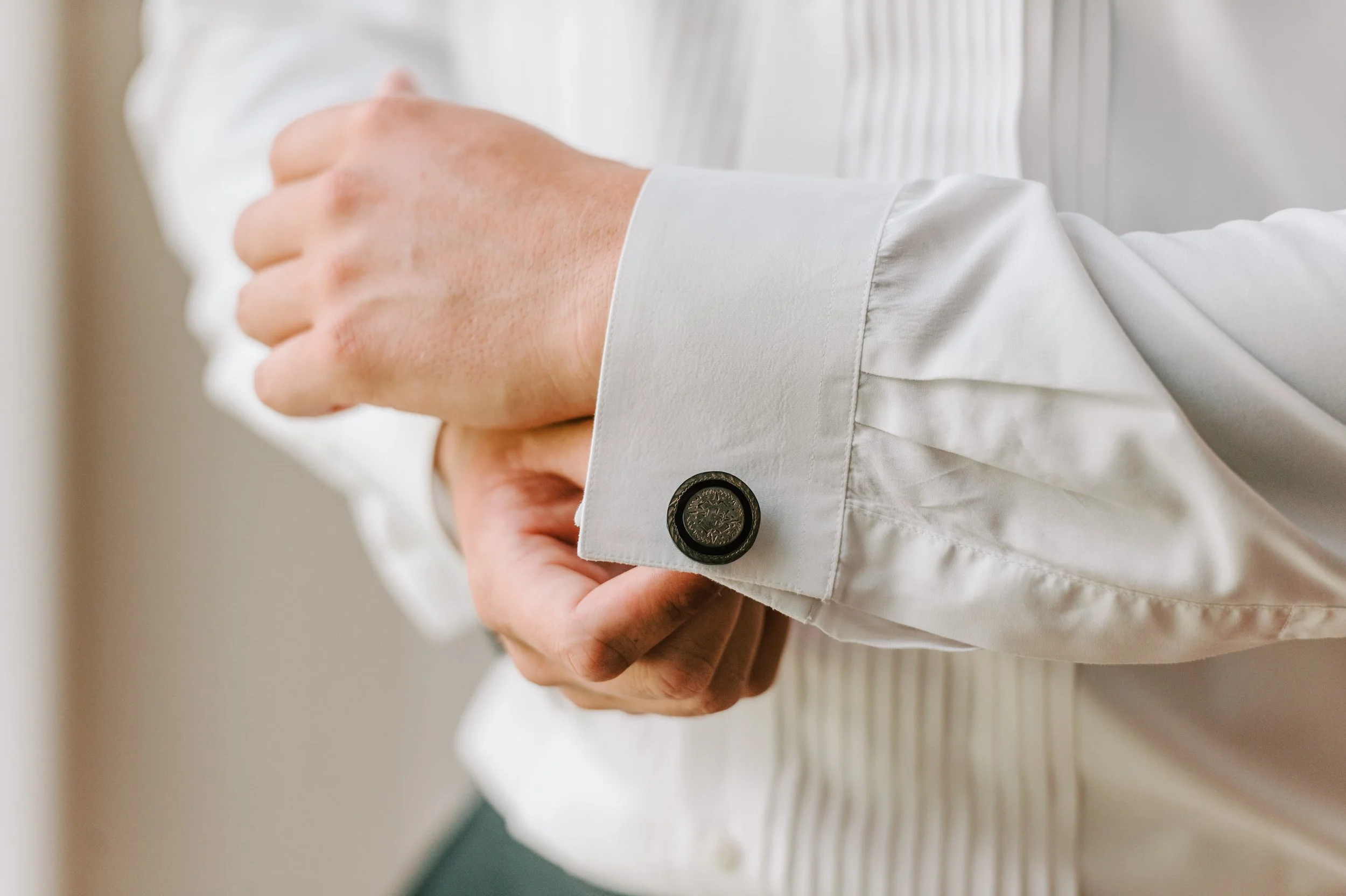 A person adjusting cufflinks on a white dress shirt.