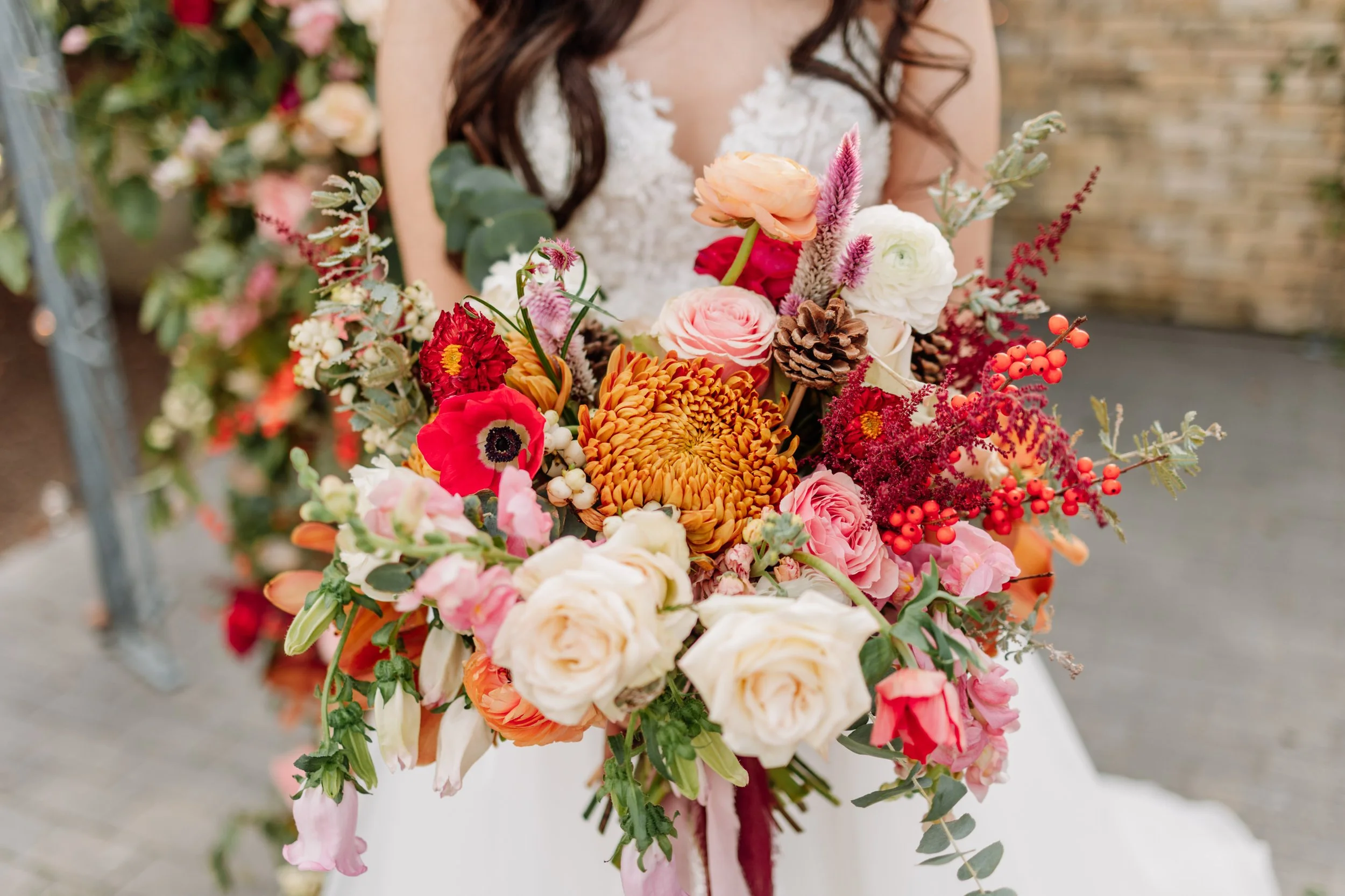 A person in a dress holding a large bouquet of colorful flowers, including roses, dahlias, and berries.