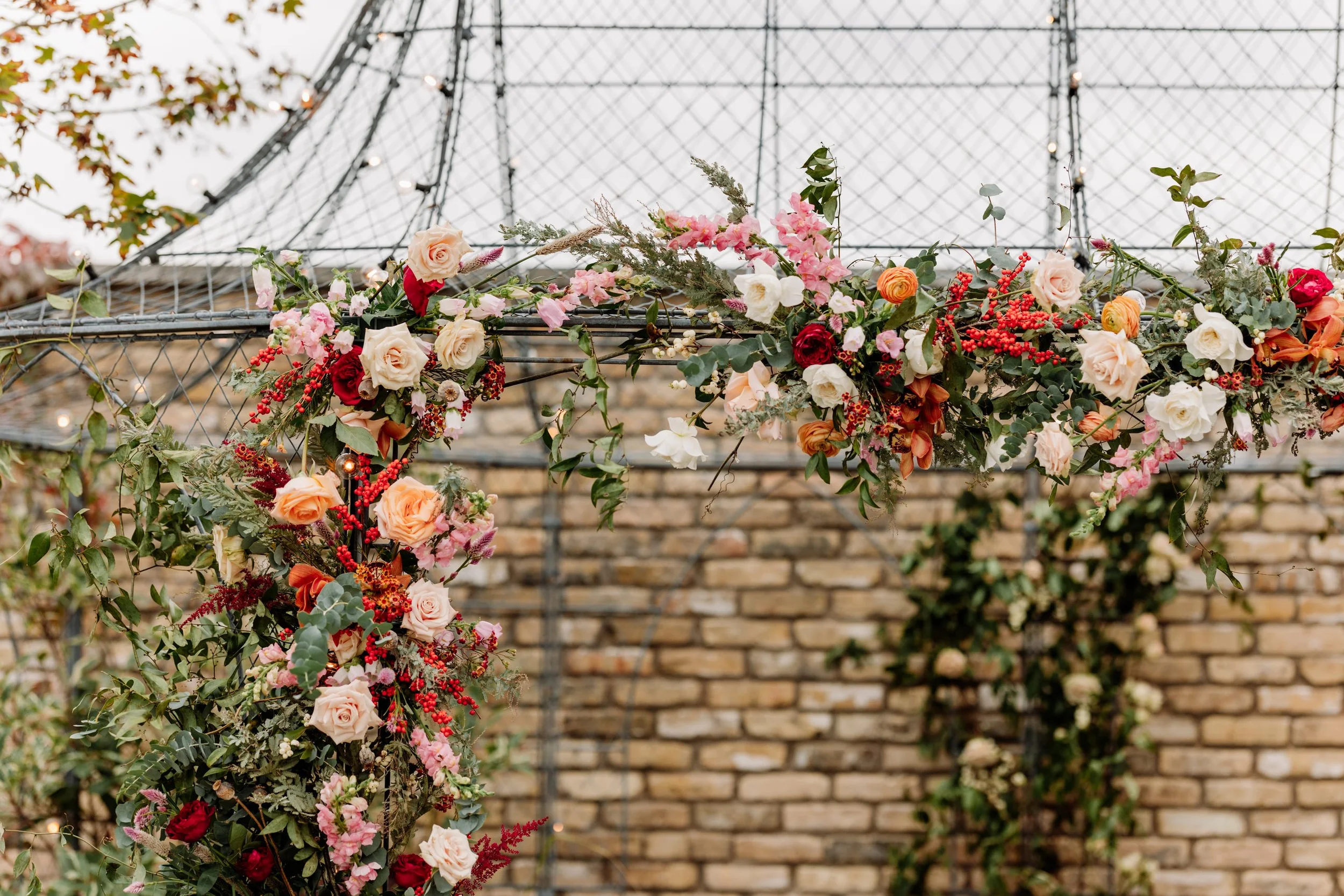 Floral decoration with roses and other flowers hanging on a metal structure against a brick wall.