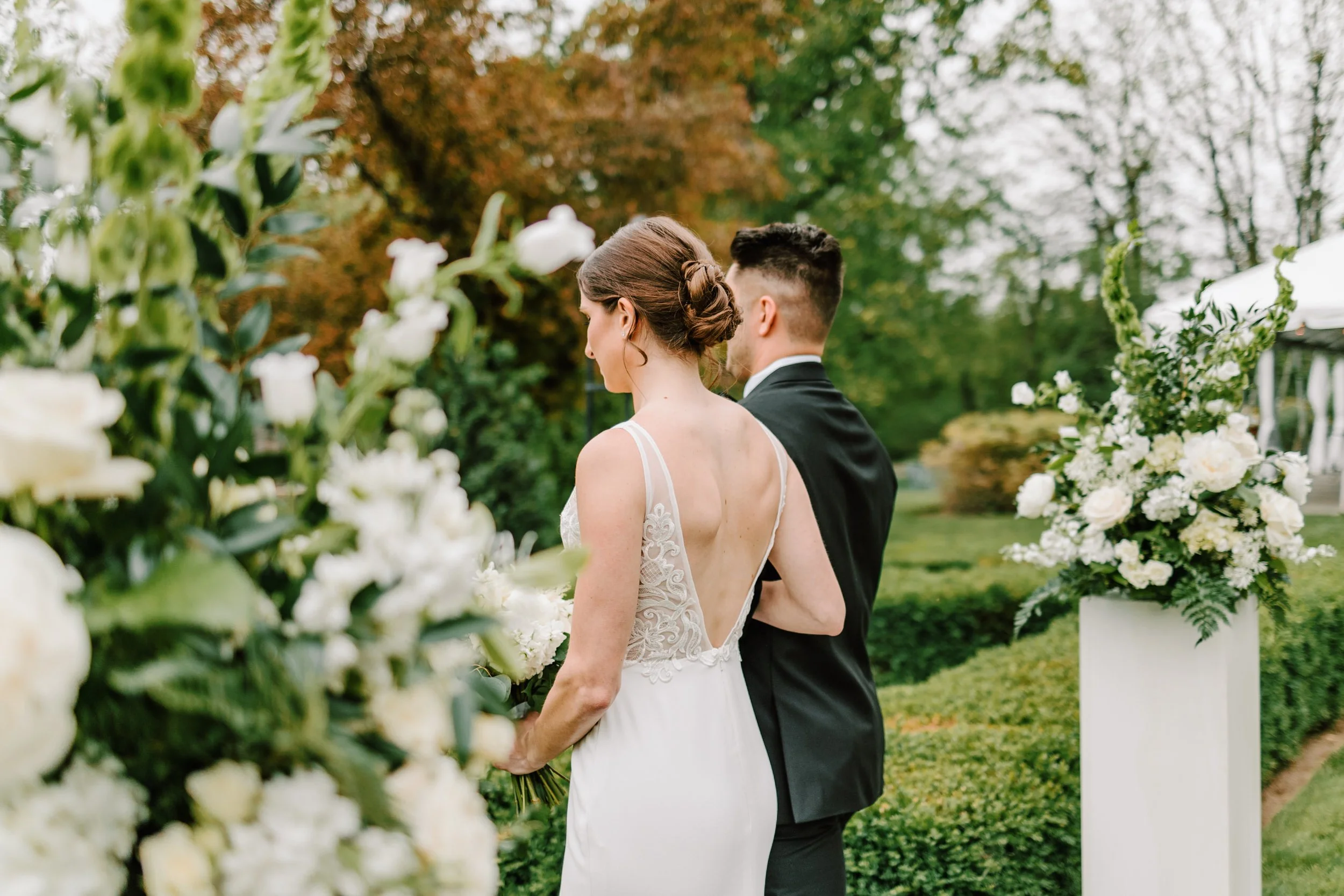 A bride and groom standing outdoors near white flower arrangements during a wedding ceremony.