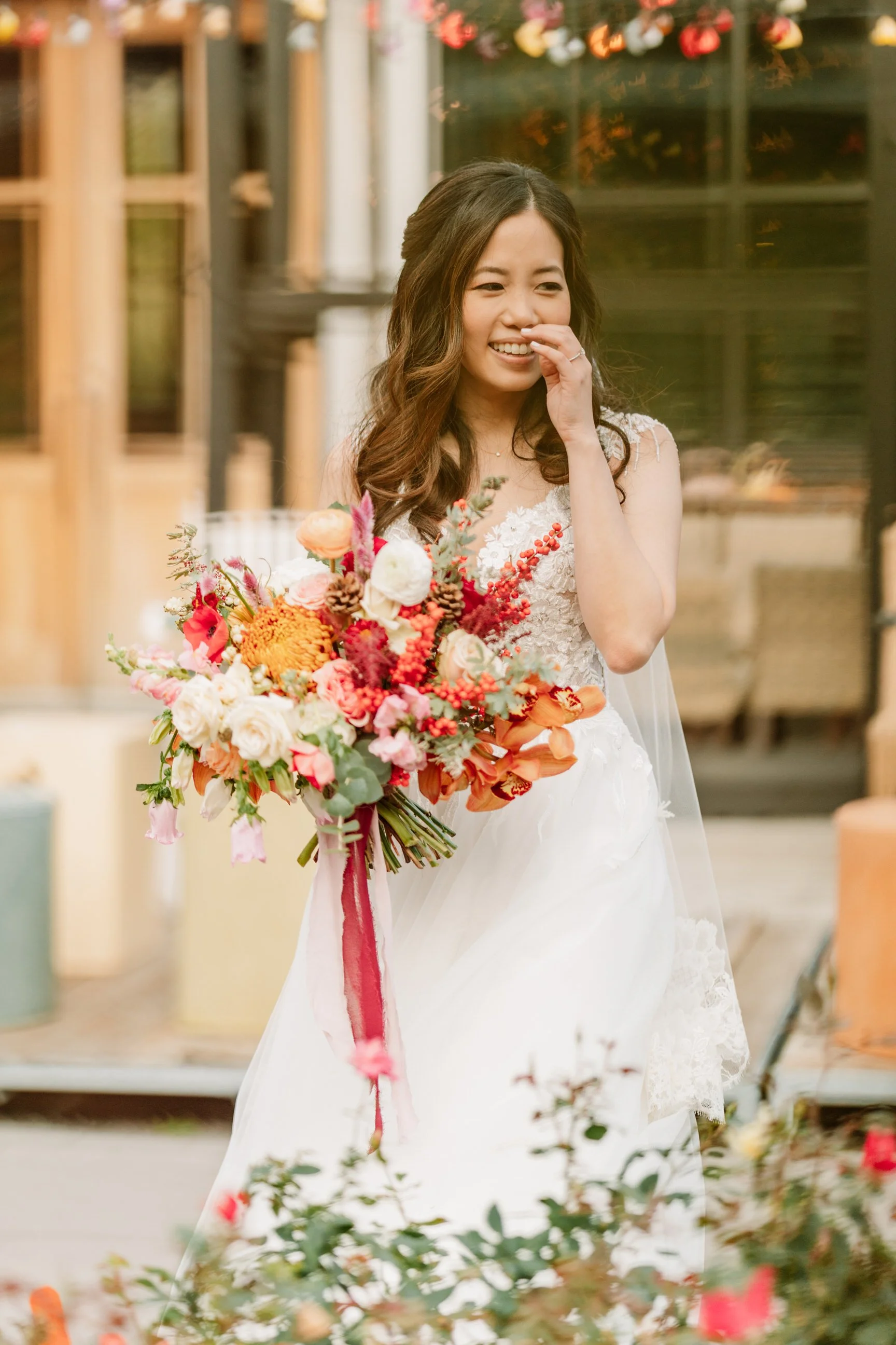 A bride in a white wedding dress holding a bouquet of colorful flowers and smiling.