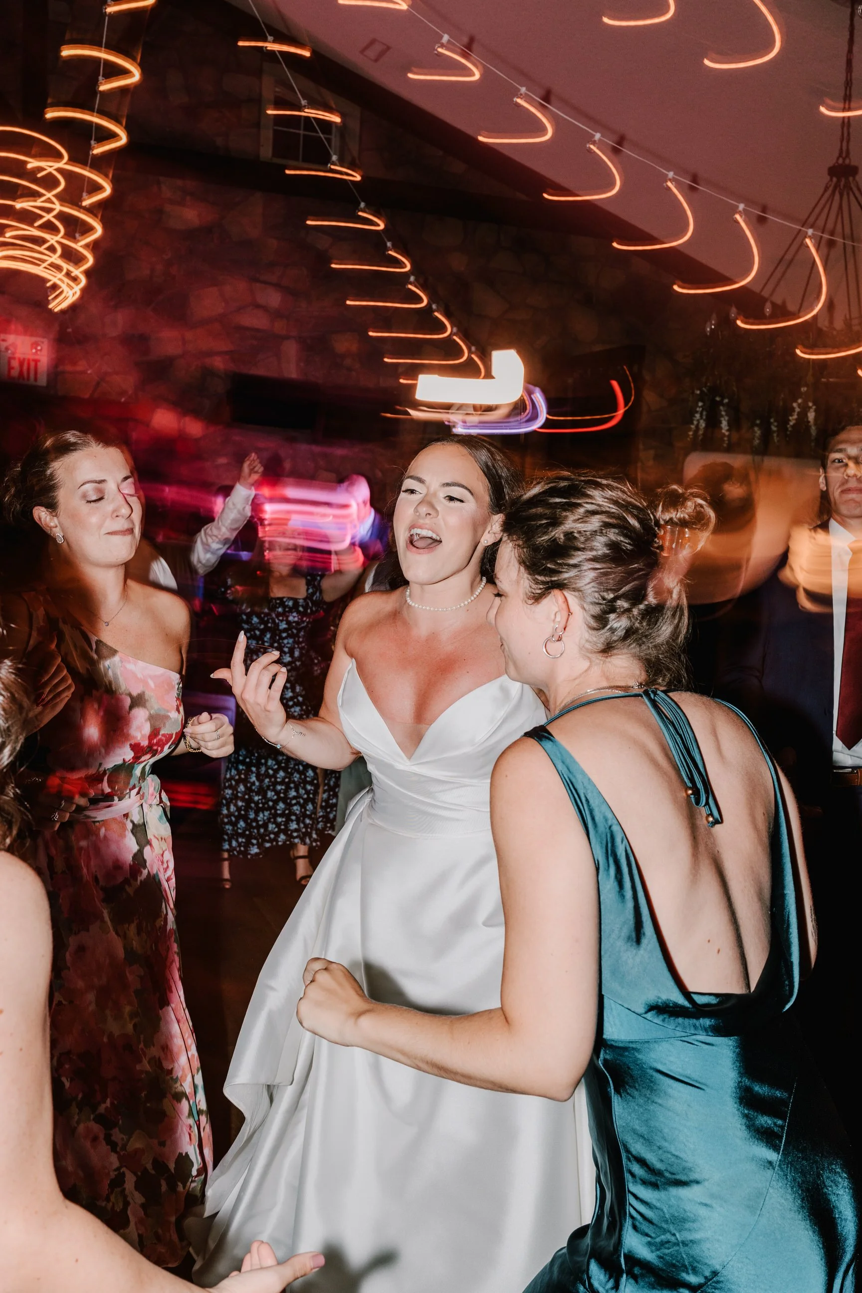 Group of people dancing and celebrating at a wedding reception, with colorful lights and motion blur effects.