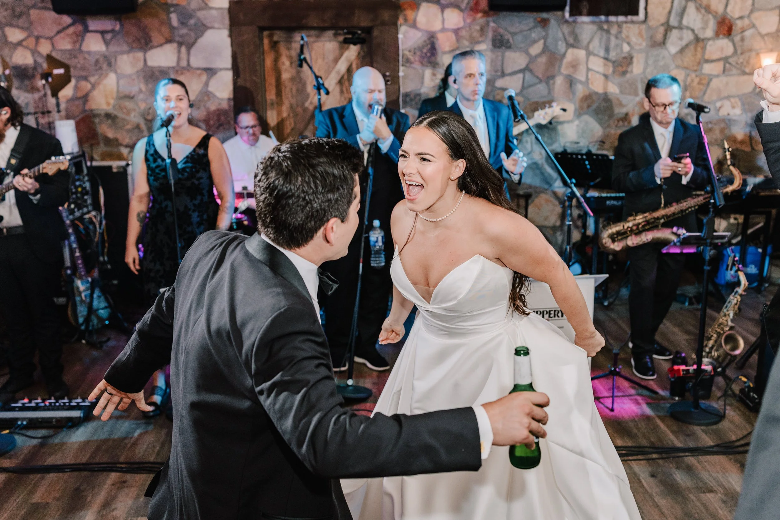 A bride and groom dancing and singing together at their wedding reception with a live band in the background.