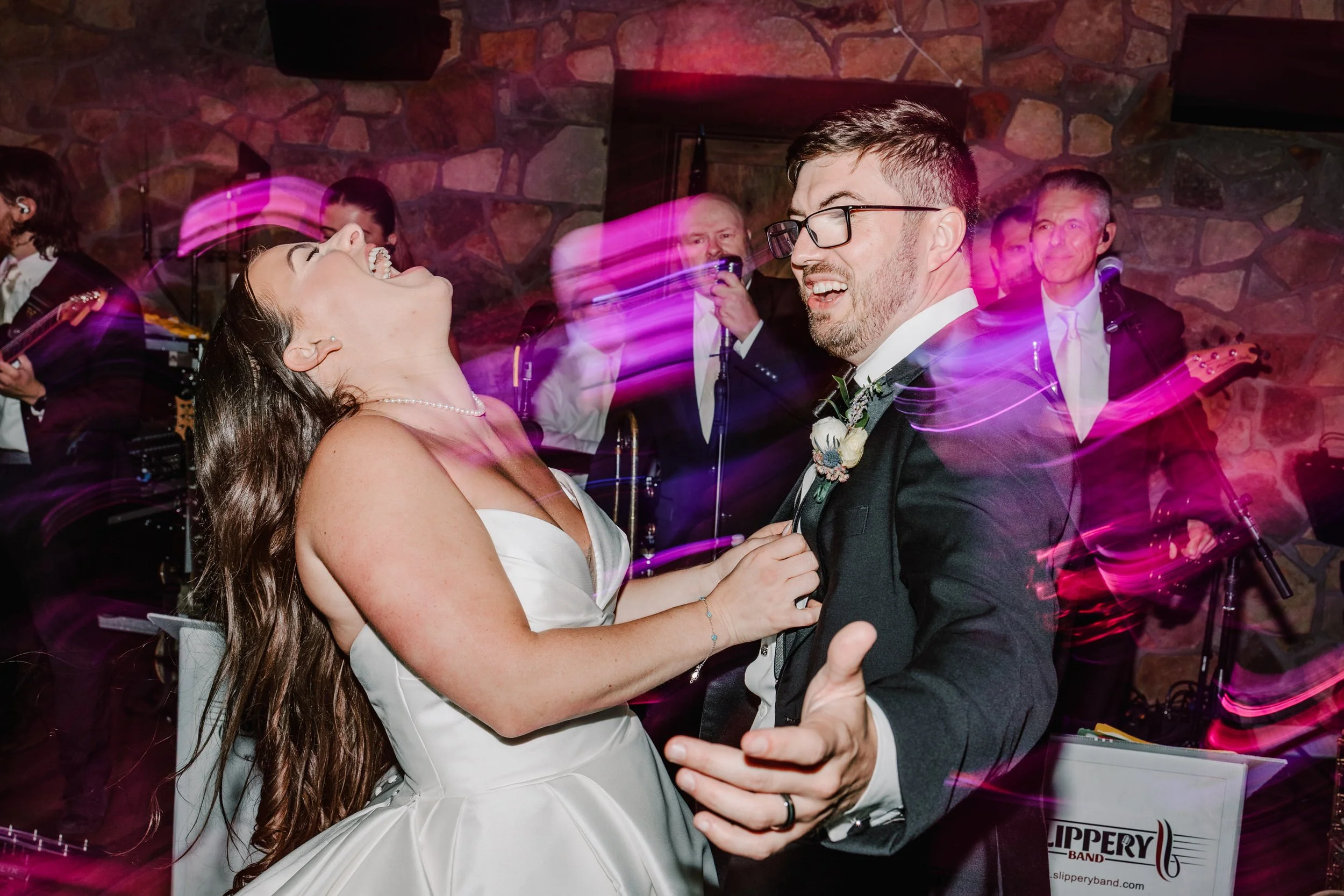 A bride and groom are dancing and laughing at their wedding reception while a band plays in the background.