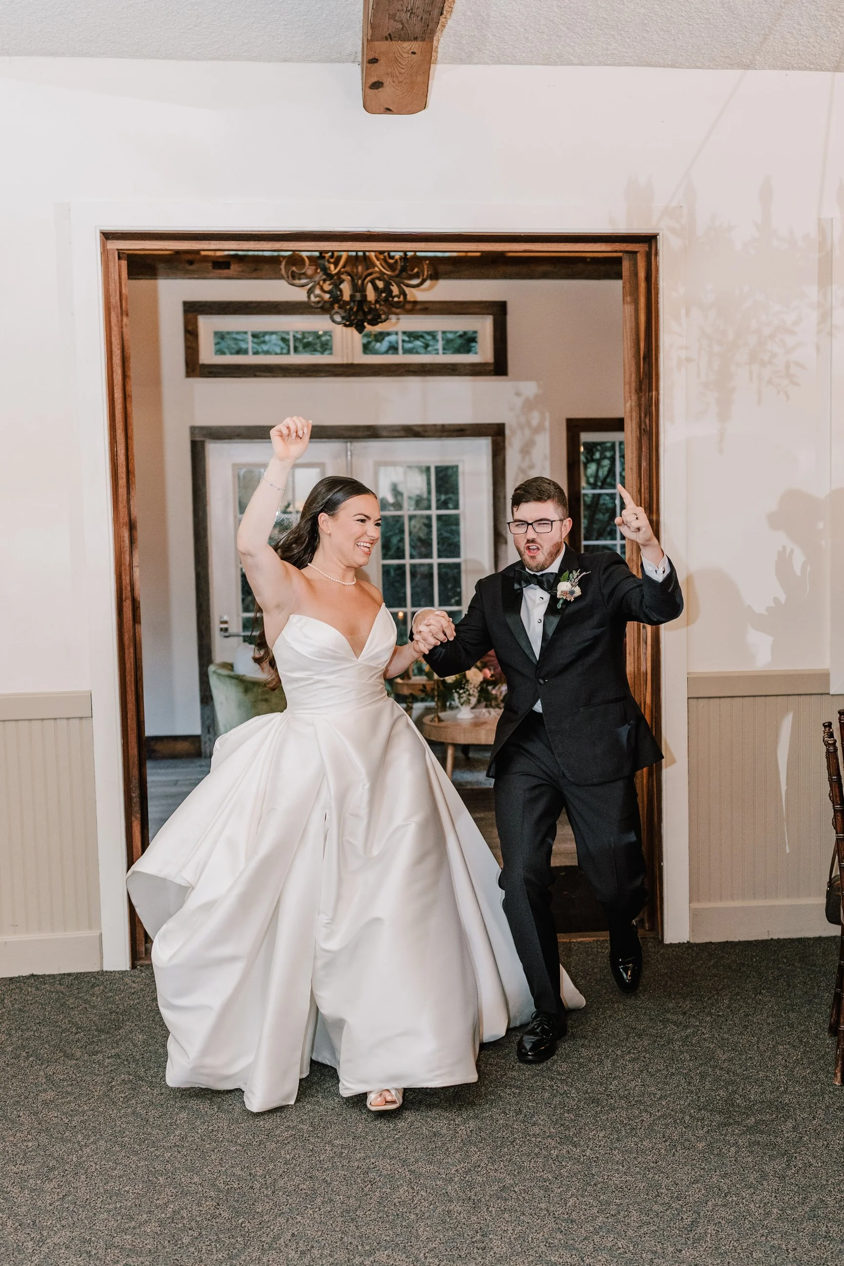 A bride and groom celebrating as they run through a doorway during their wedding reception, holding hands and smiling.